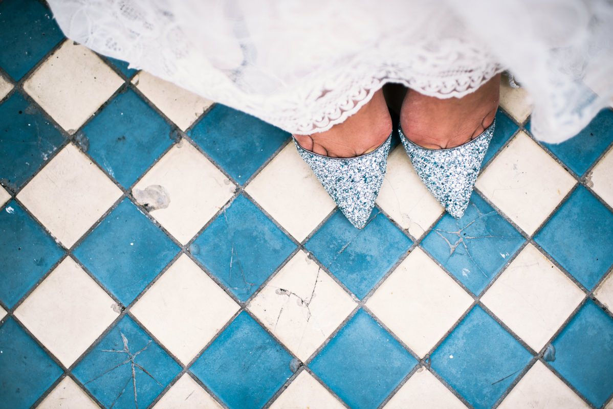 Sparkly blue bridal shoes shown on blue and white checkered floor tiles.