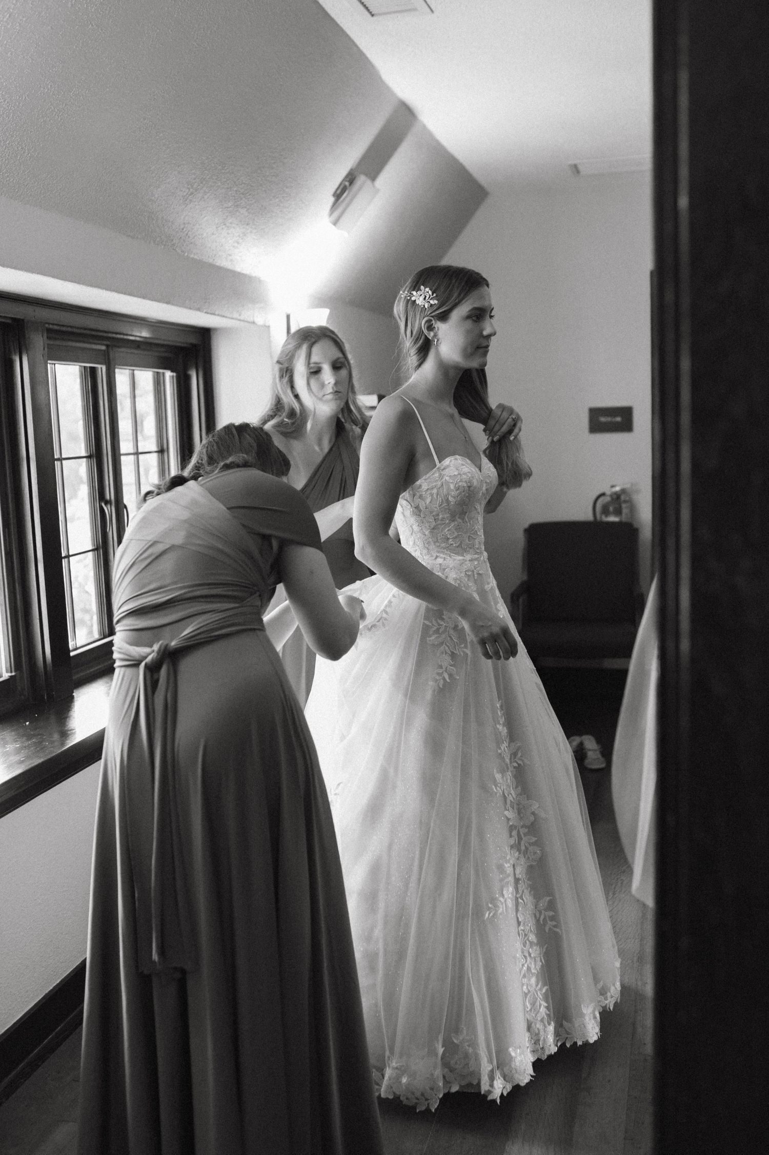 Black and white photo of bride getting help with wedding dress preparations.