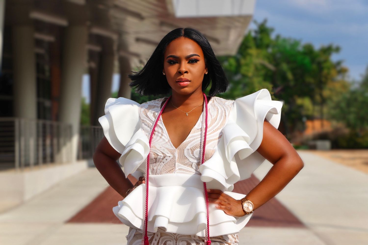 Woman in elegant white ruffled dress poses confidently outside a building with palm trees in the background.