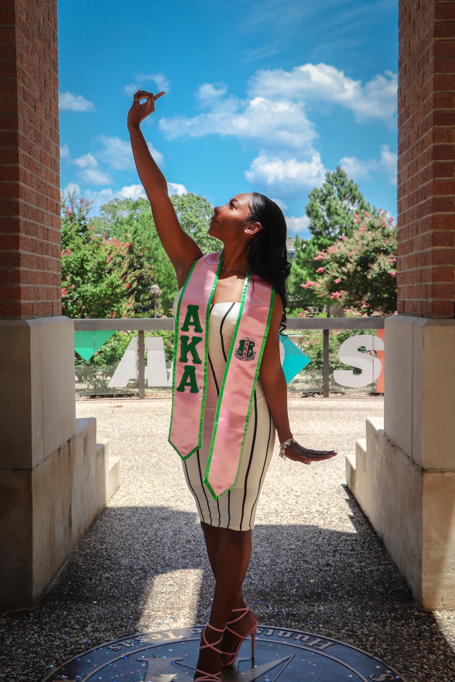 Dramatic pose in striped dress between brick columns with blue sky background.