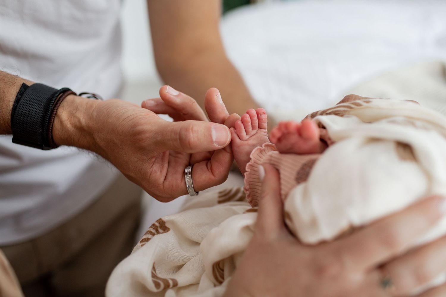 Close-up shot of tiny baby feet being gently held by adult hands against white fabric.