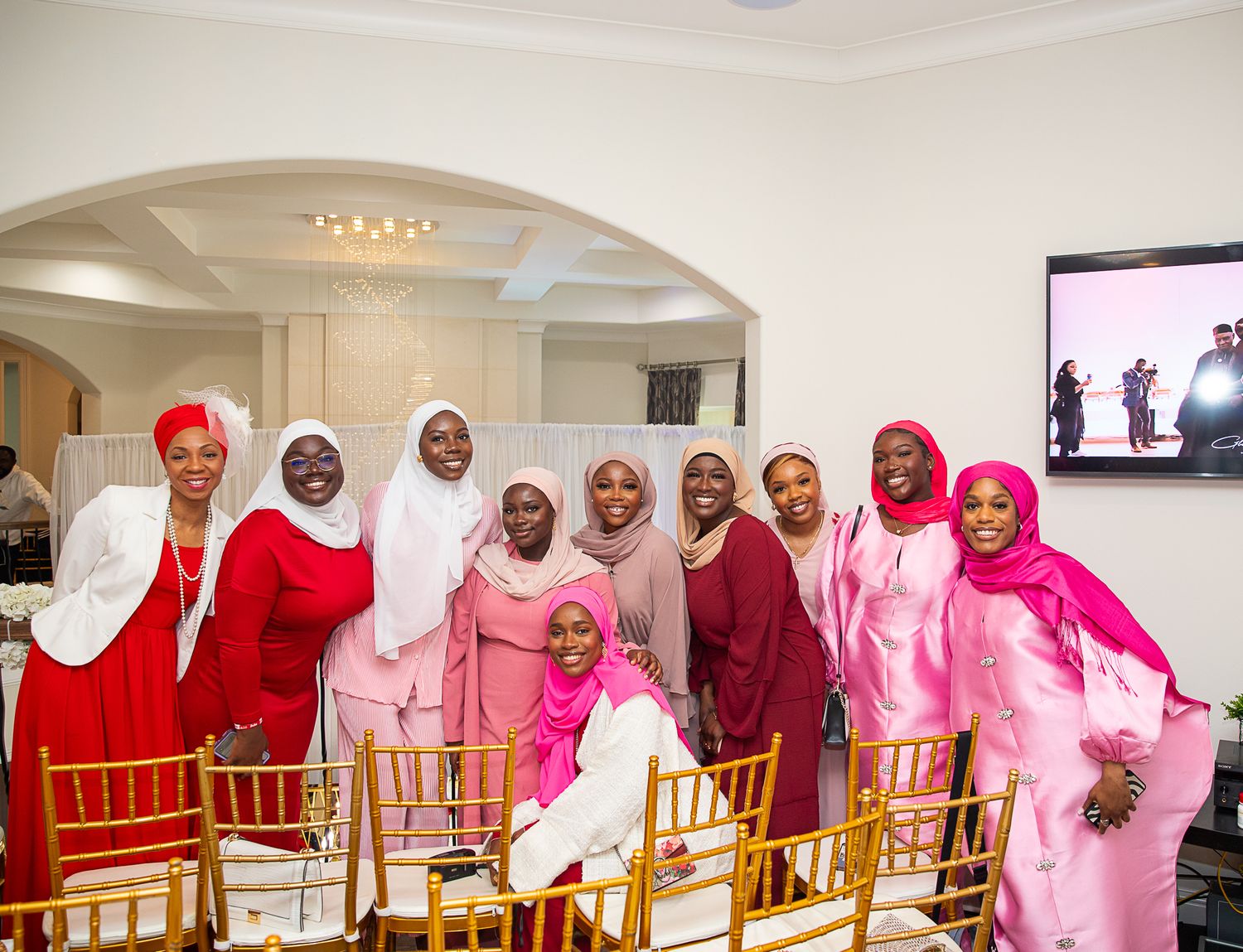 Group gathering in colorful traditional attire featuring white, pink, and red hijabs.