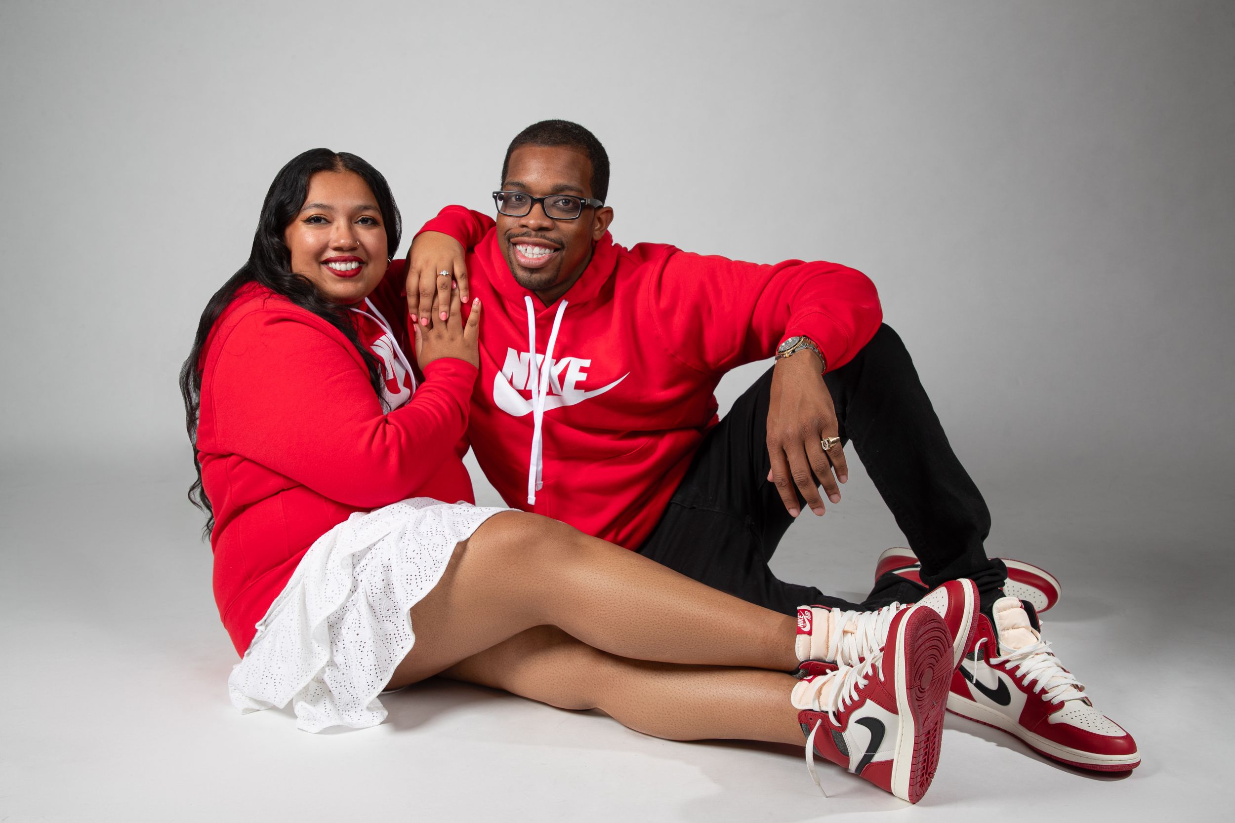 A casual photoshoot with matching red Nike hoodies and sneakers against a white studio background.