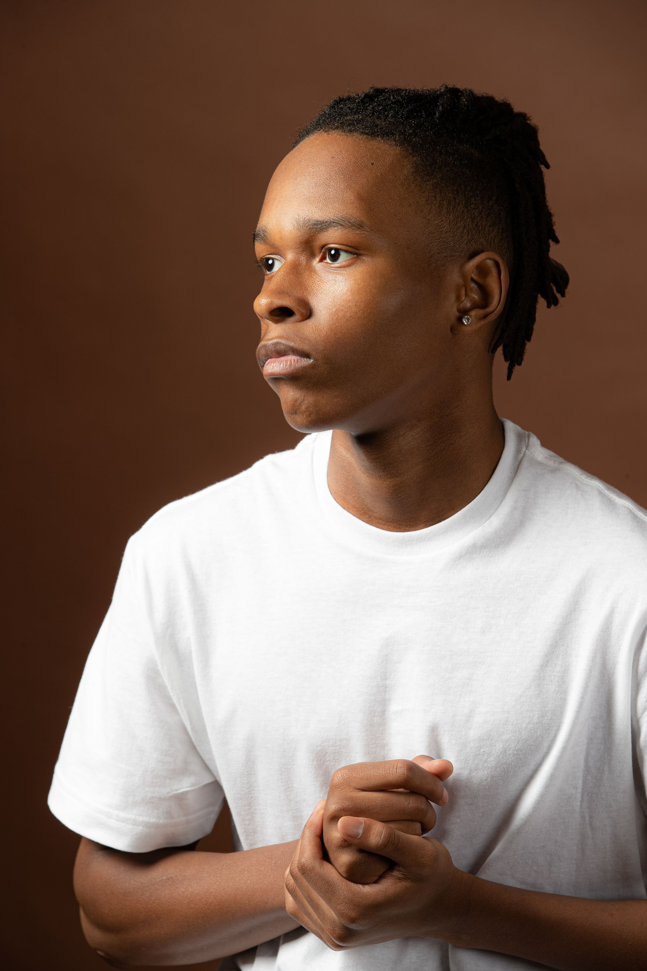 Studio portrait against brown background showing contemplative pose in white t-shirt with natural lighting.