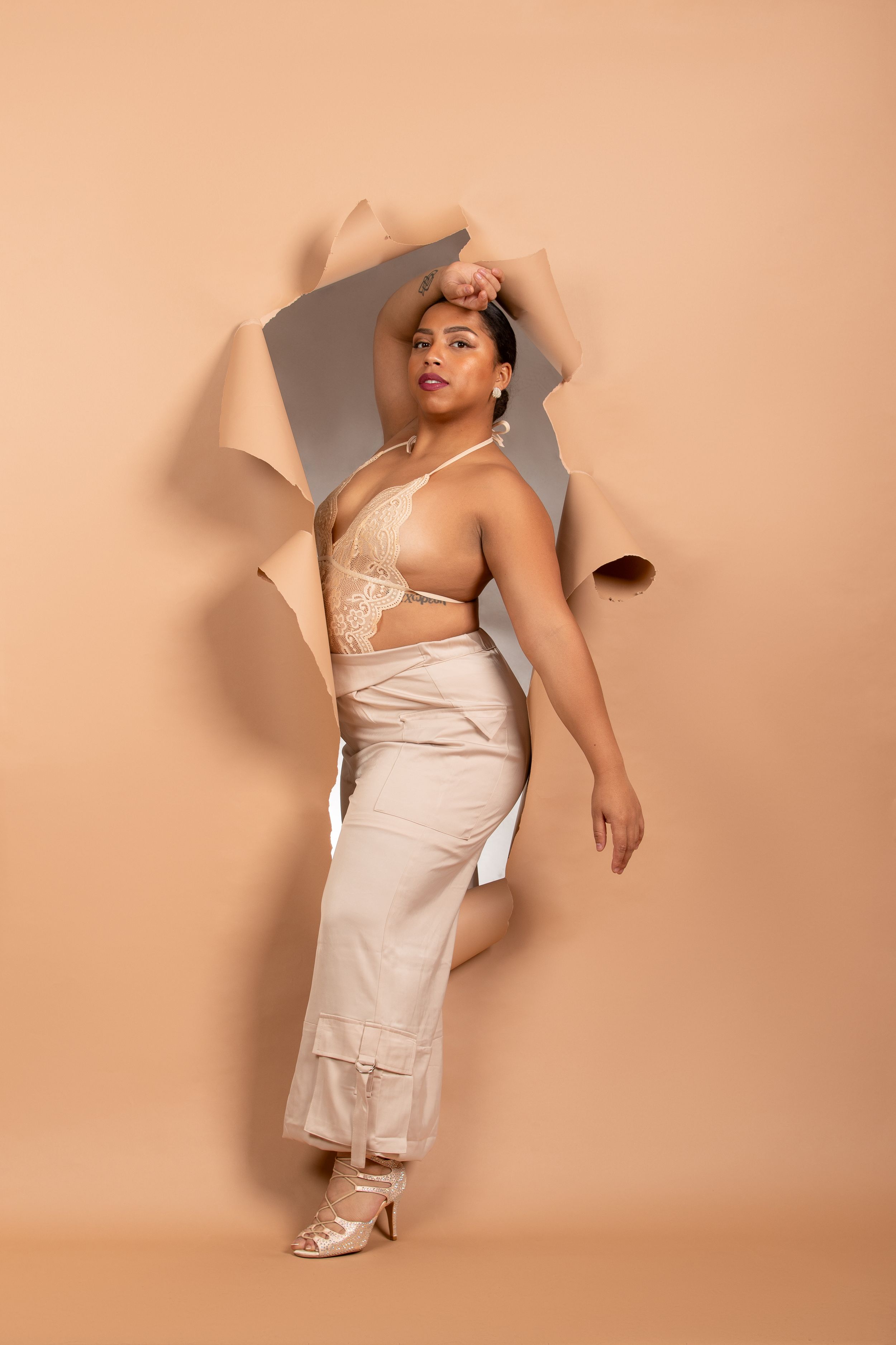 A stylish fashion portrait featuring a cream-colored outfit against a torn paper peach backdrop.
