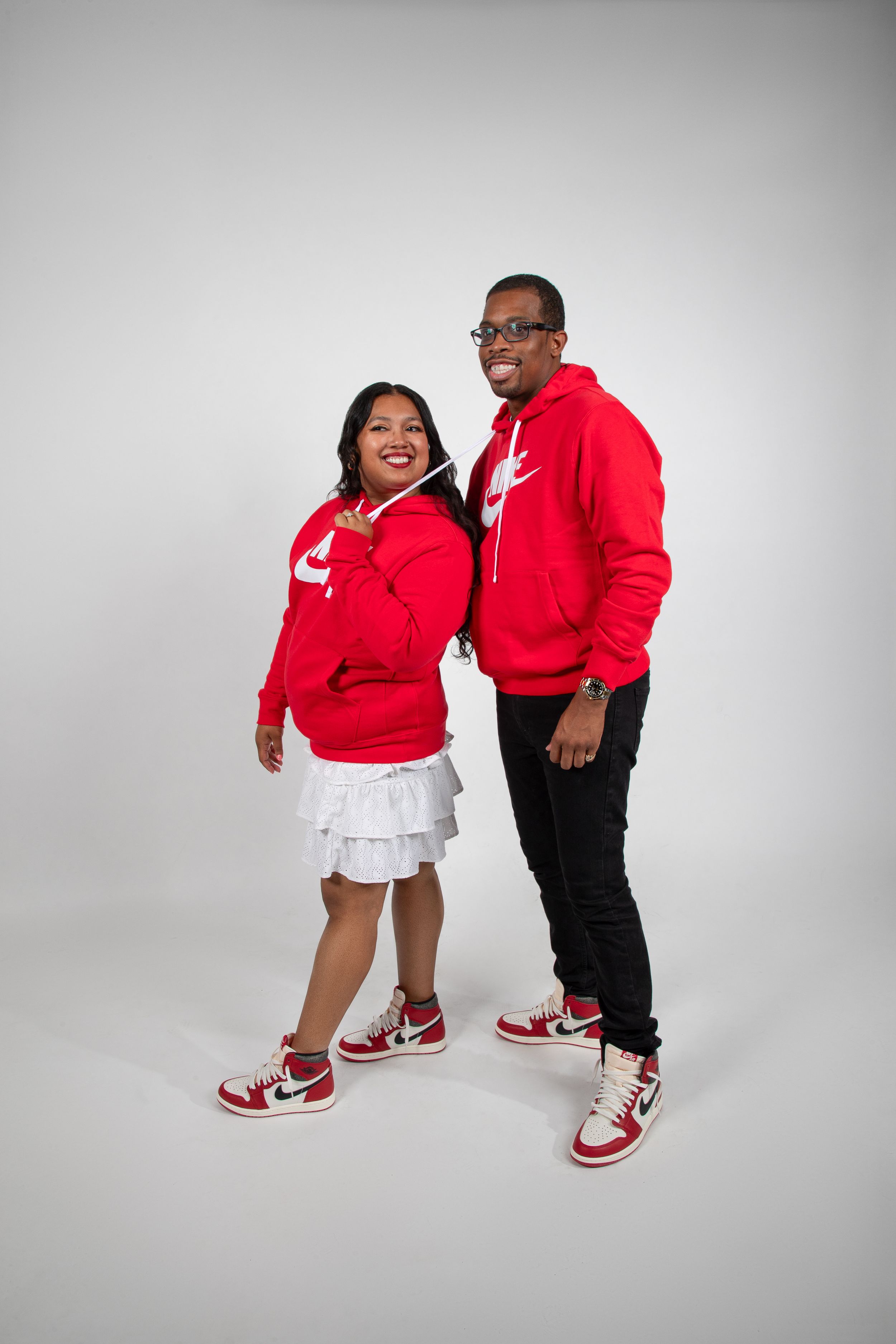 A standing portrait of two people in matching red Nike hoodies and sneakers on white background.