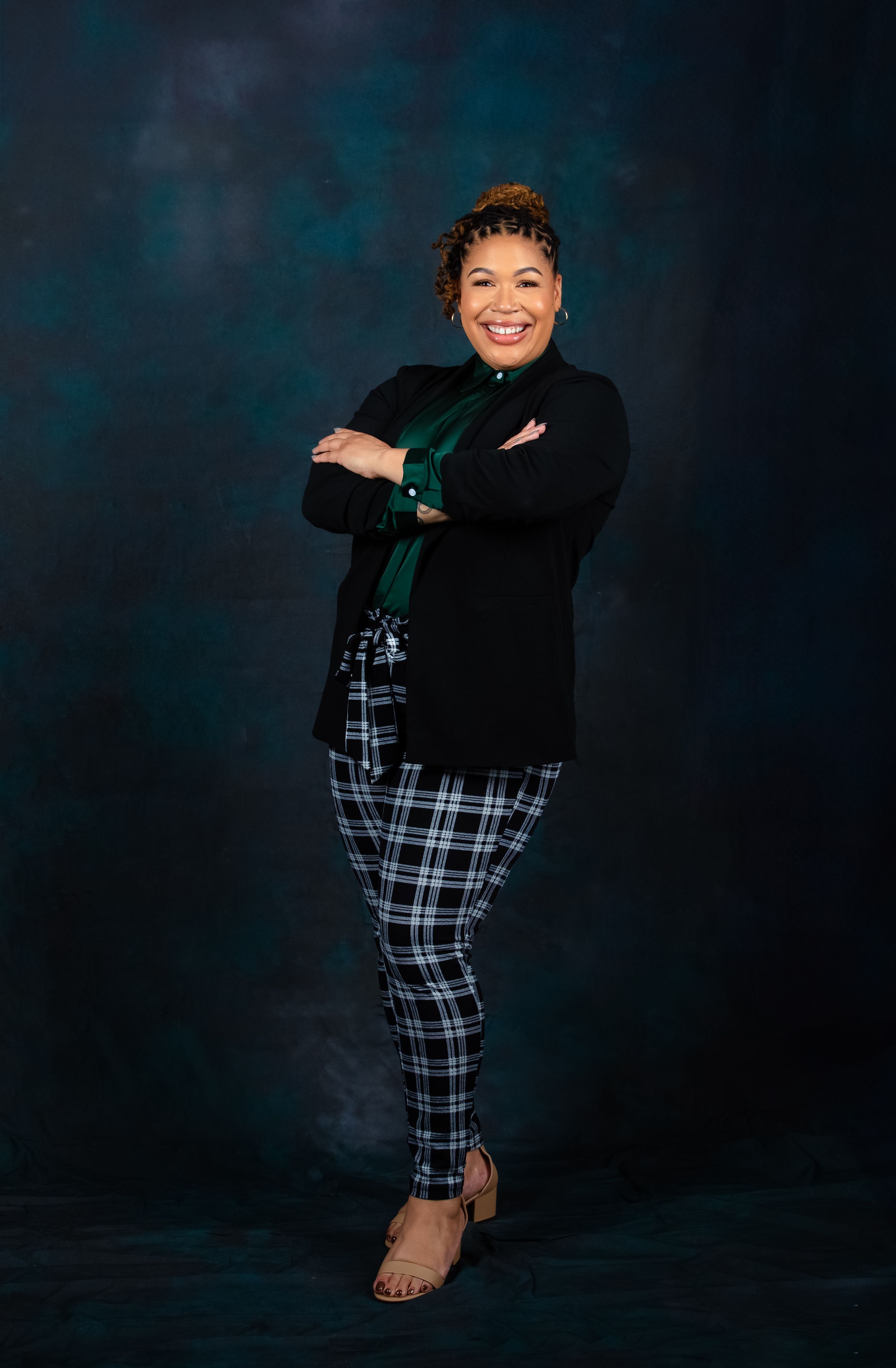 A studio portrait featuring plaid pants and a black sweater against a dark blue textured background.