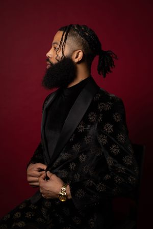 Profile view of person in luxurious patterned black blazer against deep red background.