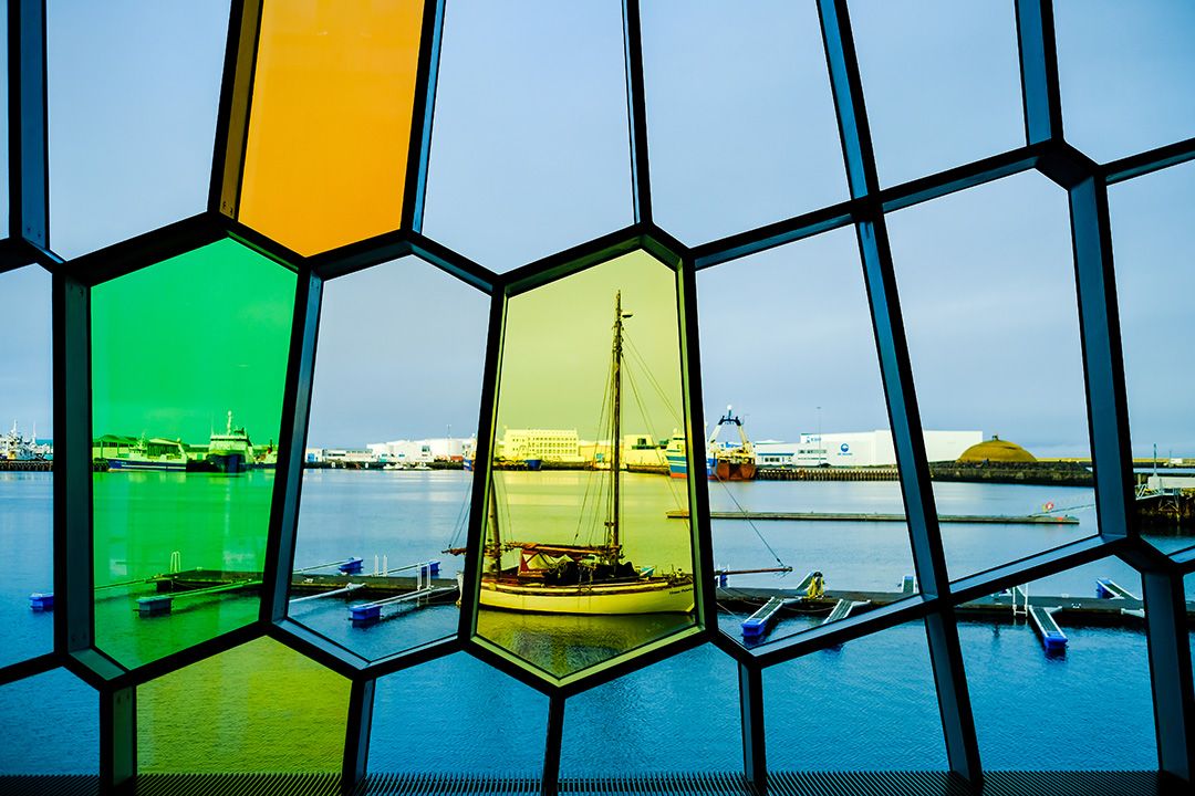 Colorful stained glass window with geometric patterns framing boats on water.