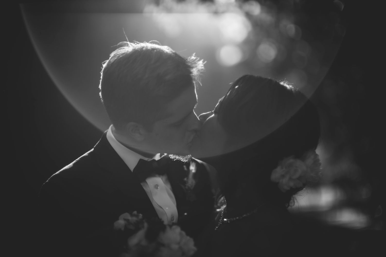 A black and white silhouette of newlyweds sharing an intimate moment with lens flare.