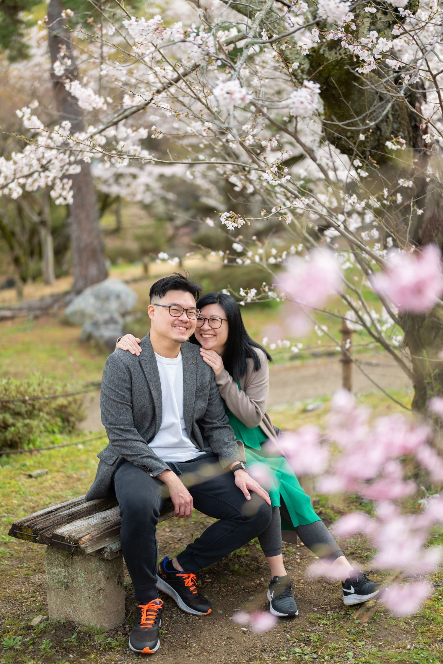 Couple sitting on bench under white cherry blossom trees in a Japanese garden.