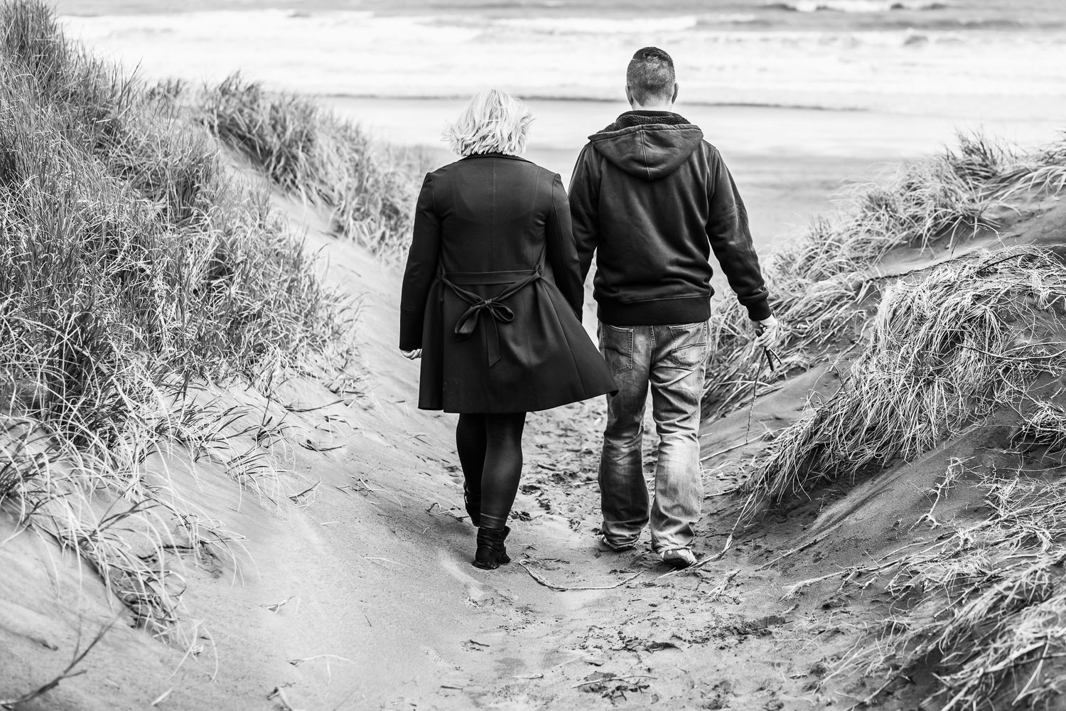 A couple holding hands entering Muriwai Beach