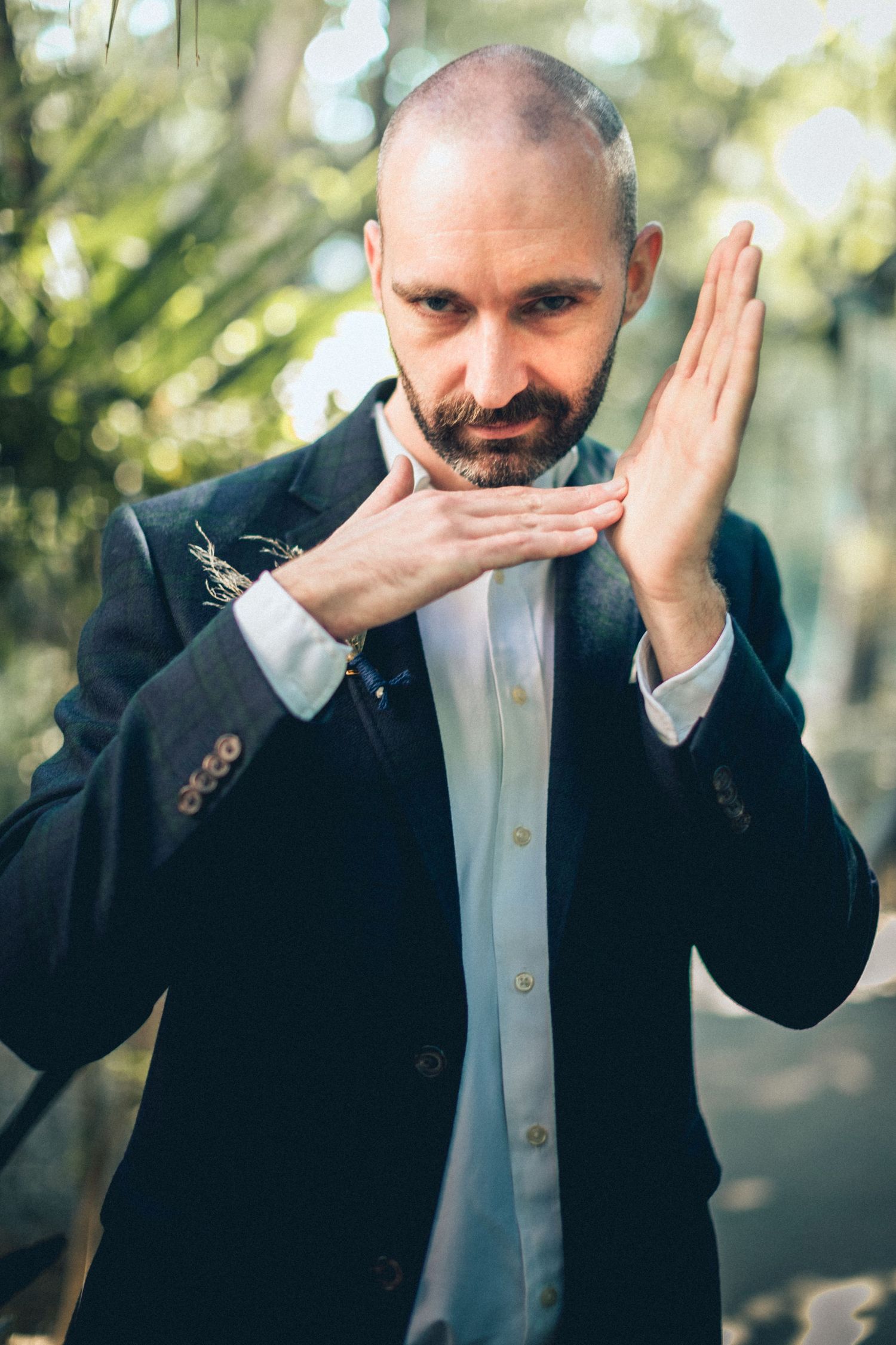 Person in suit making playful hand gesture against blurred natural background.