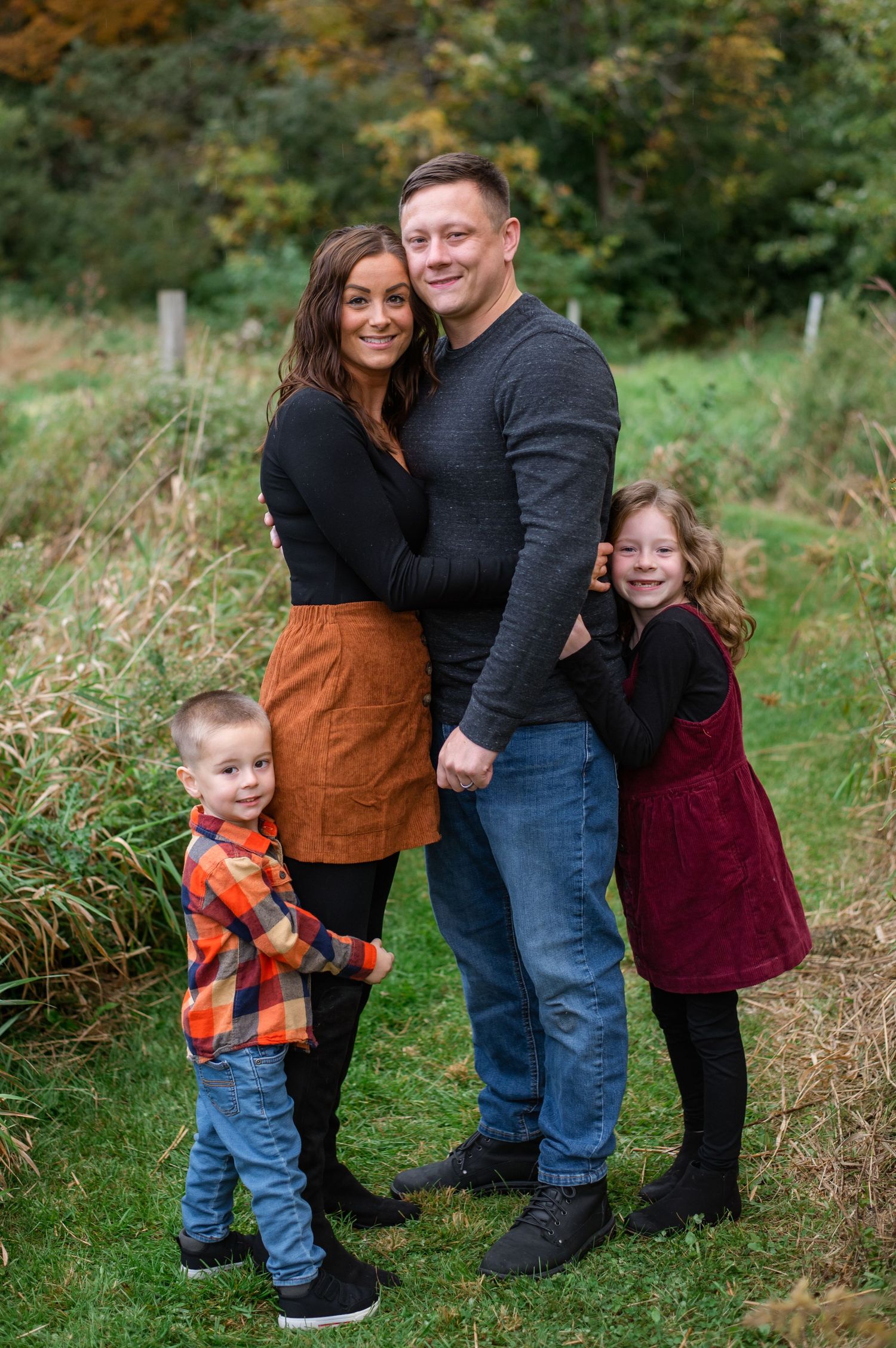 A smiling family dressed in autumn colors poses together outdoors against a natural backdrop.