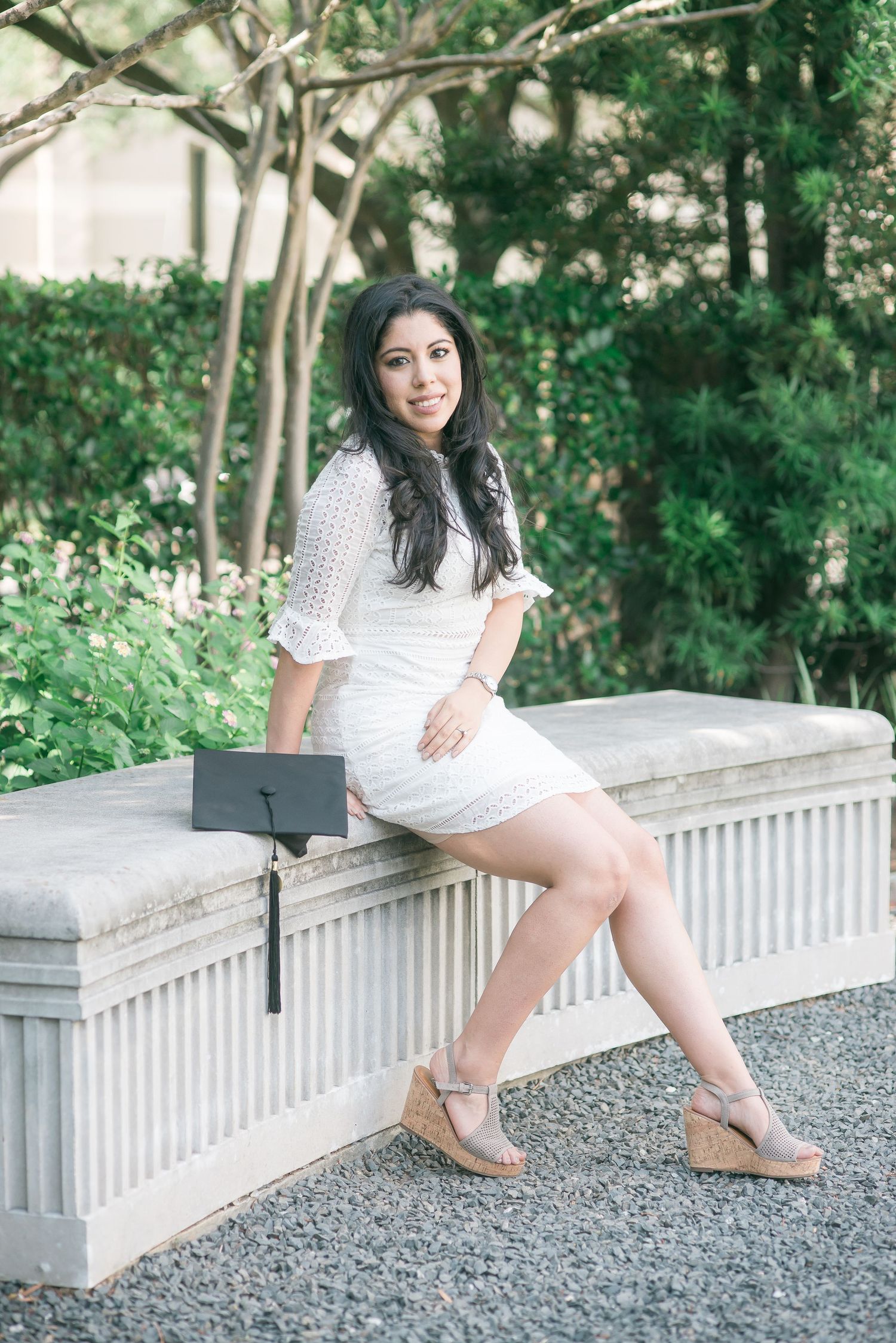 woman sitting on concrete bench in a park with her graduation cap at University of St. Thomas in Houston