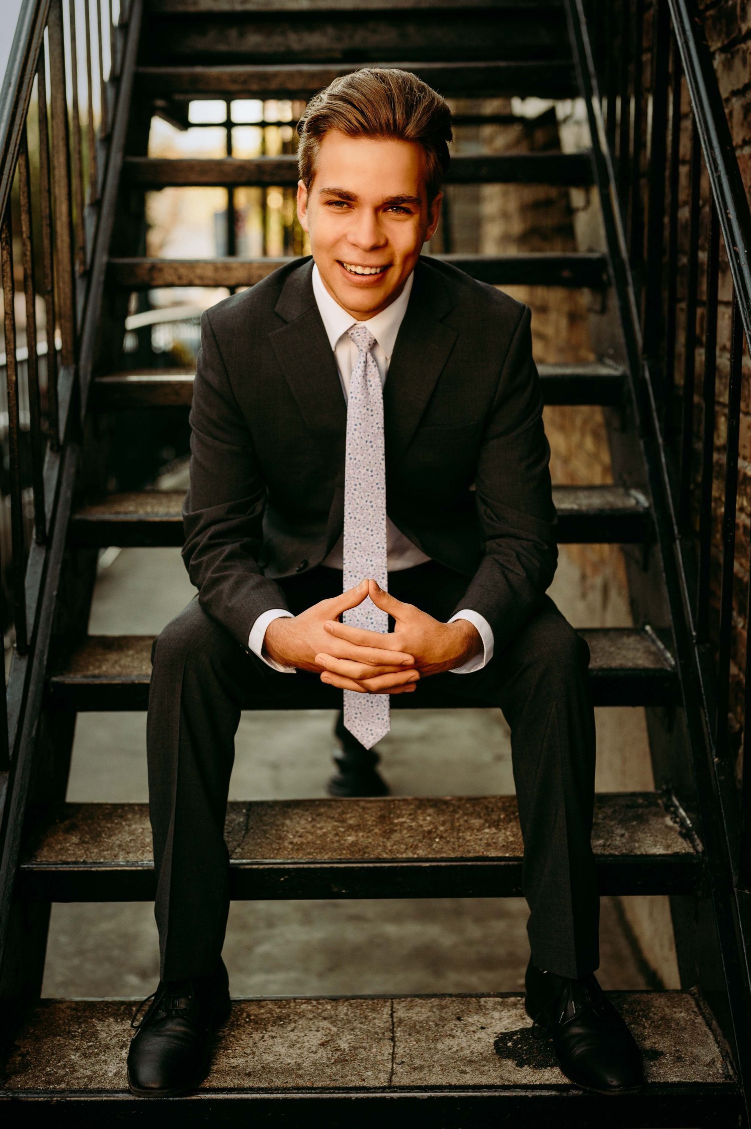 teenager guy sitting on stairs in a black suite and tie