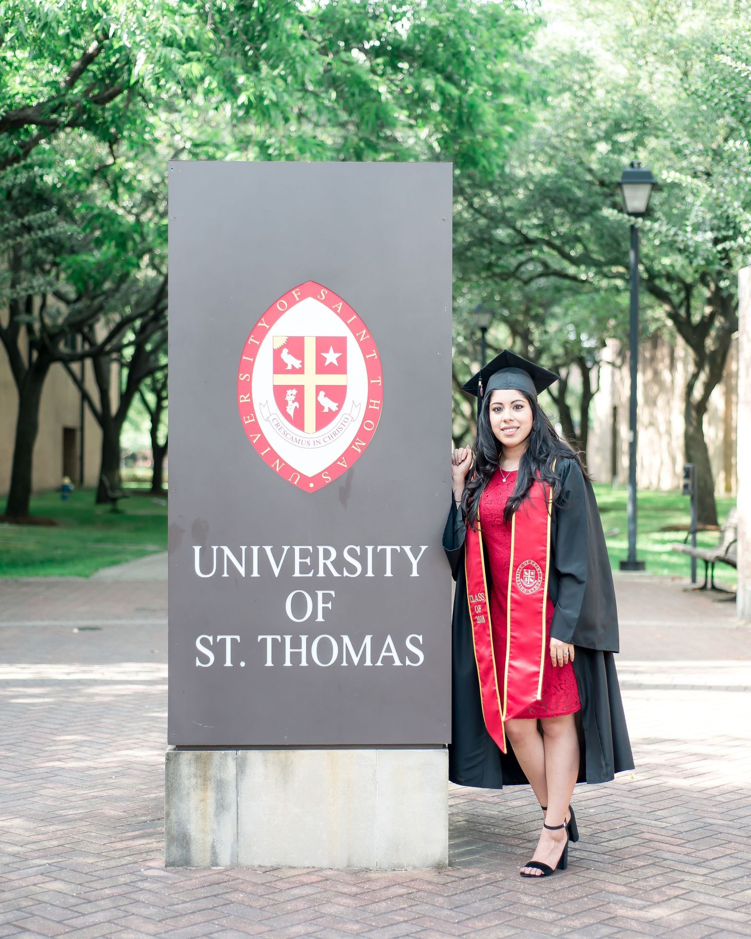 senior standing next to the University of St. Thomas sign in her cap and gown