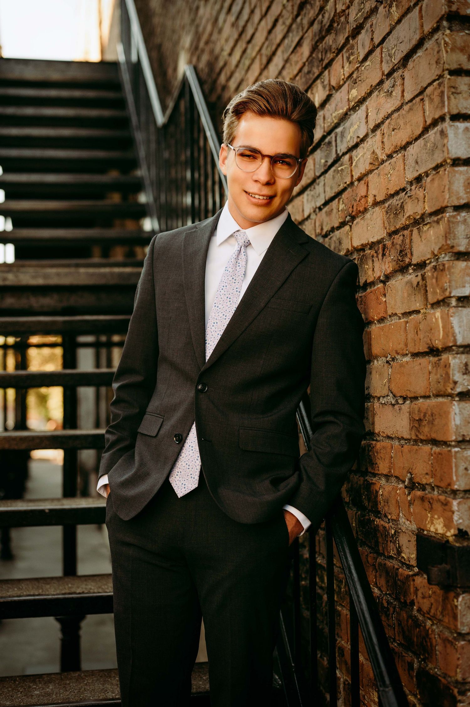 teenager in a black suit and tie leaning against a brick wall for senior portraits