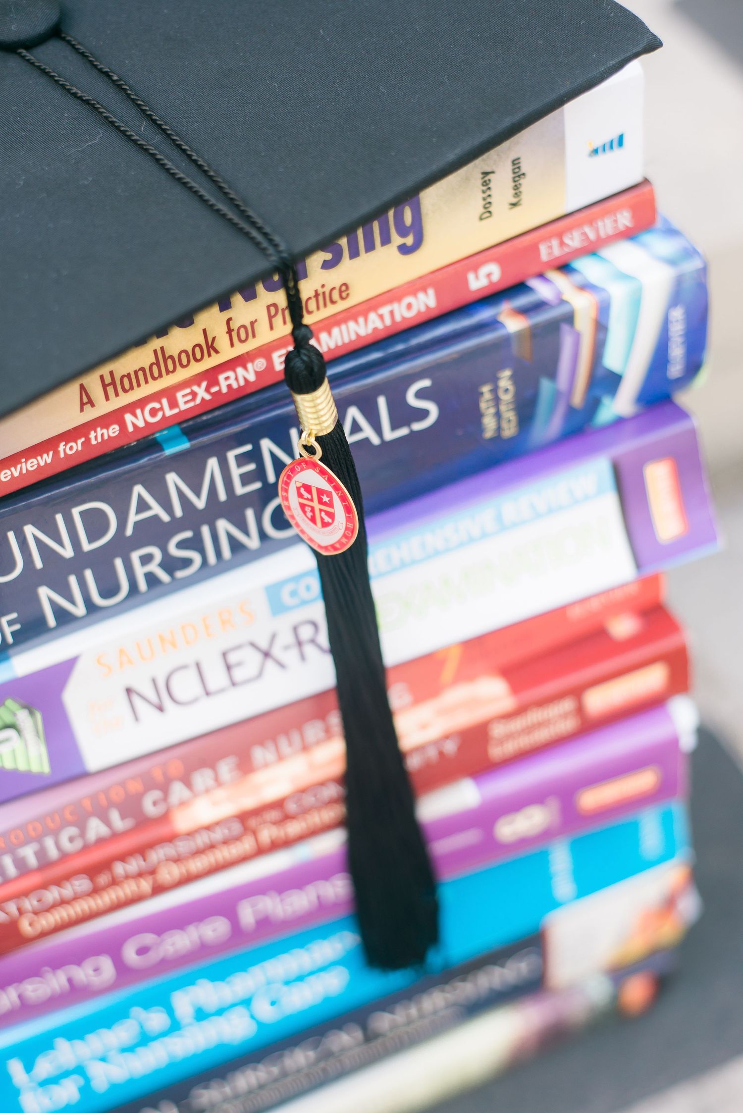 a stack of nursing college books with a graduation cap
