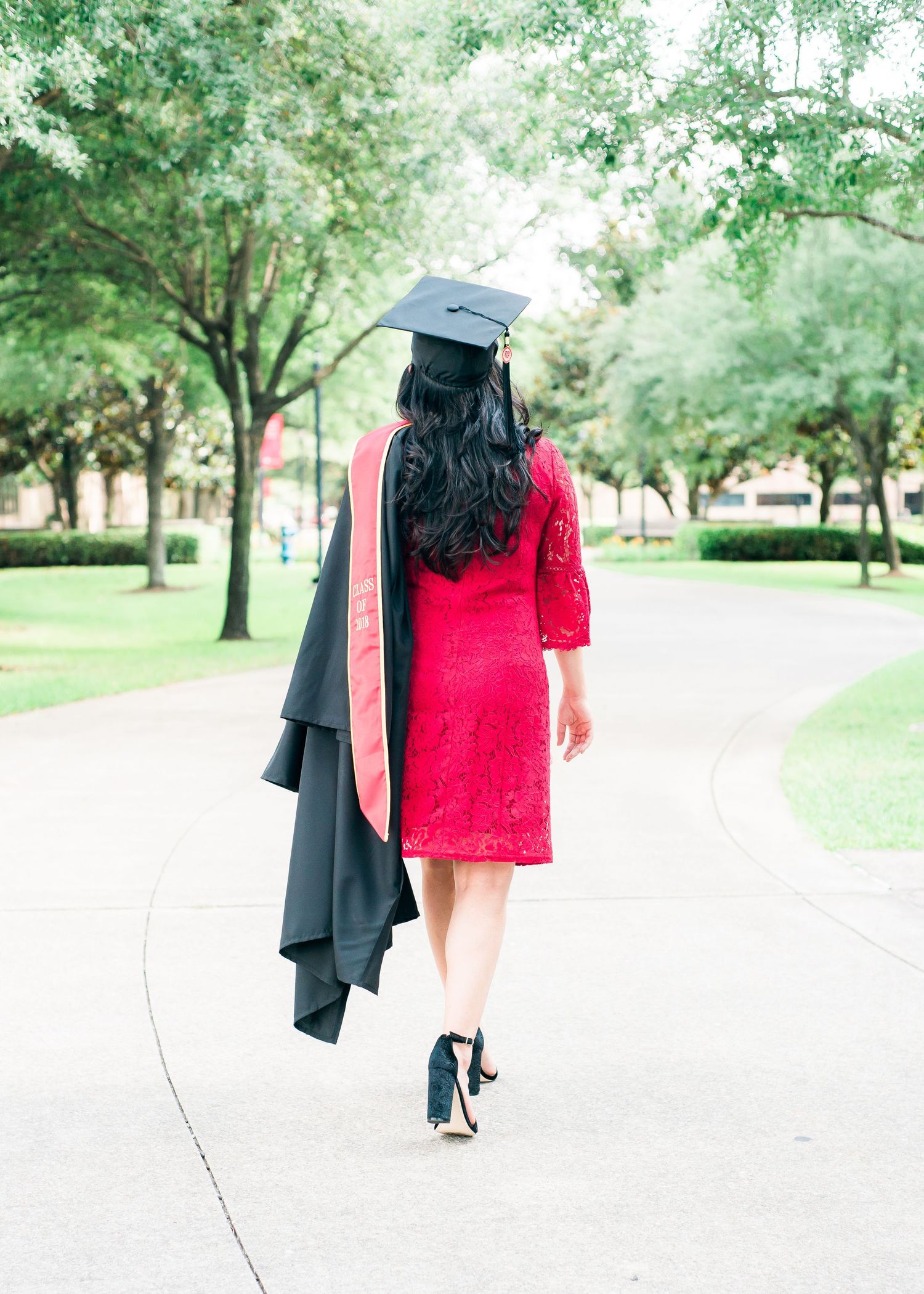 woman wearing a red dress waking away holding her graduation gown and cap