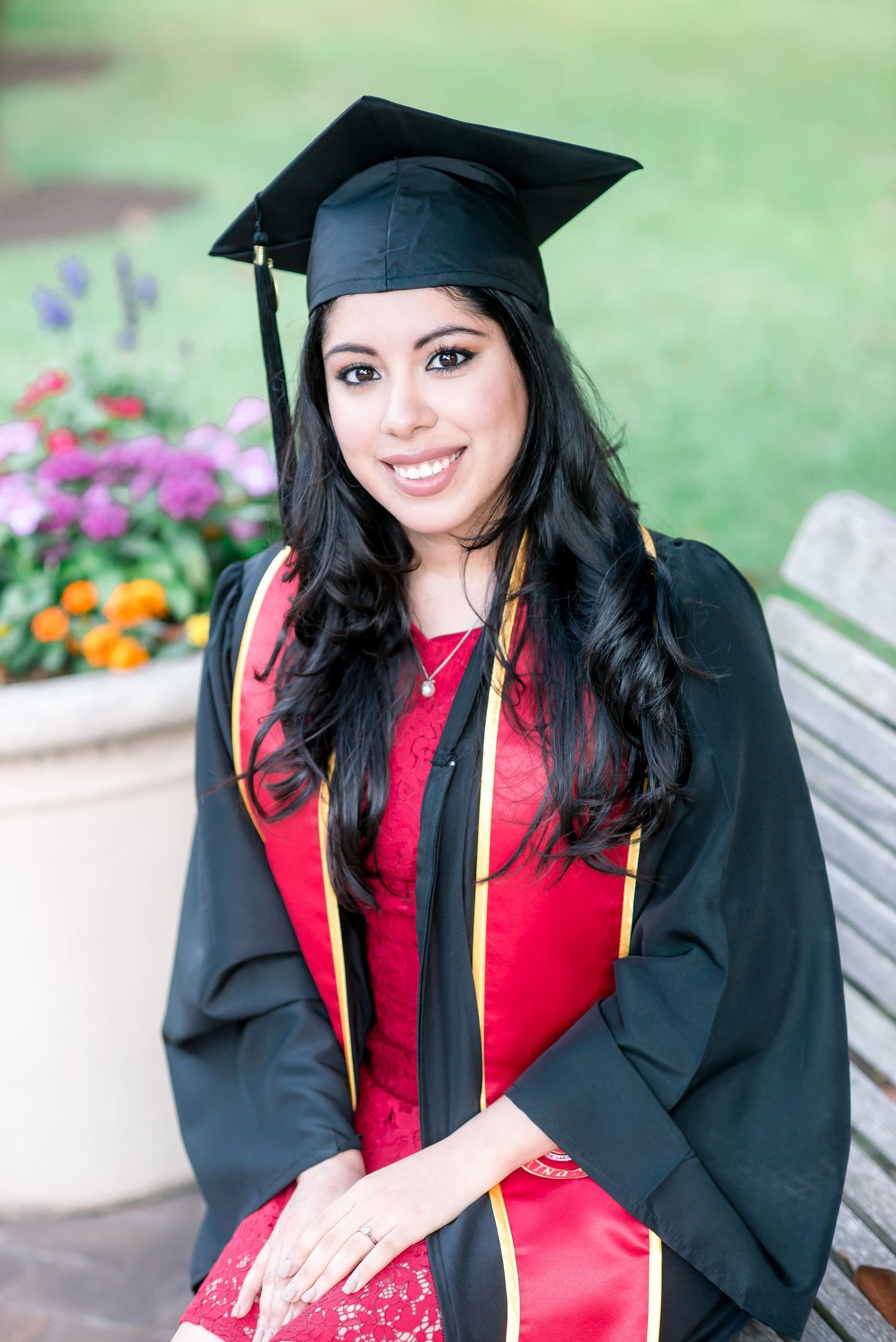 senior headshot of a woman in her cap and gown with red University of St. Thomas sash behind flowers
