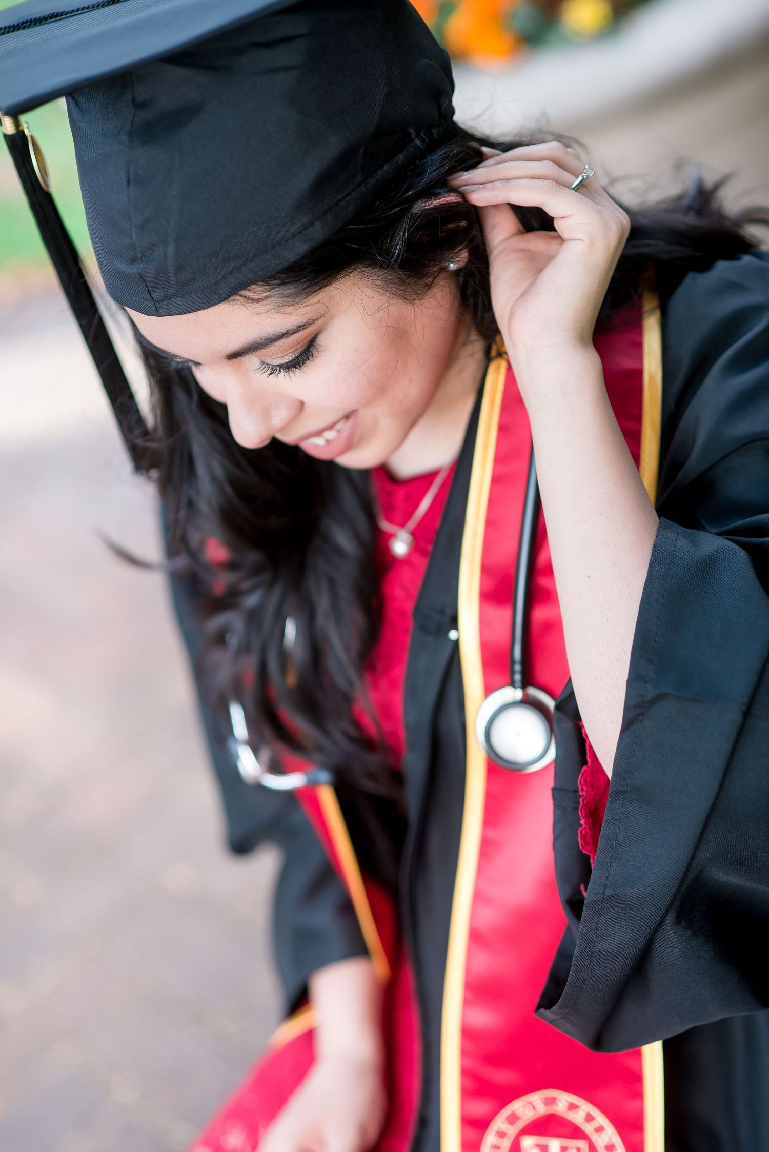 senior portrat of a rn graduate wearing her cap, gown, stethoscope, and red sash at St. Thomas University