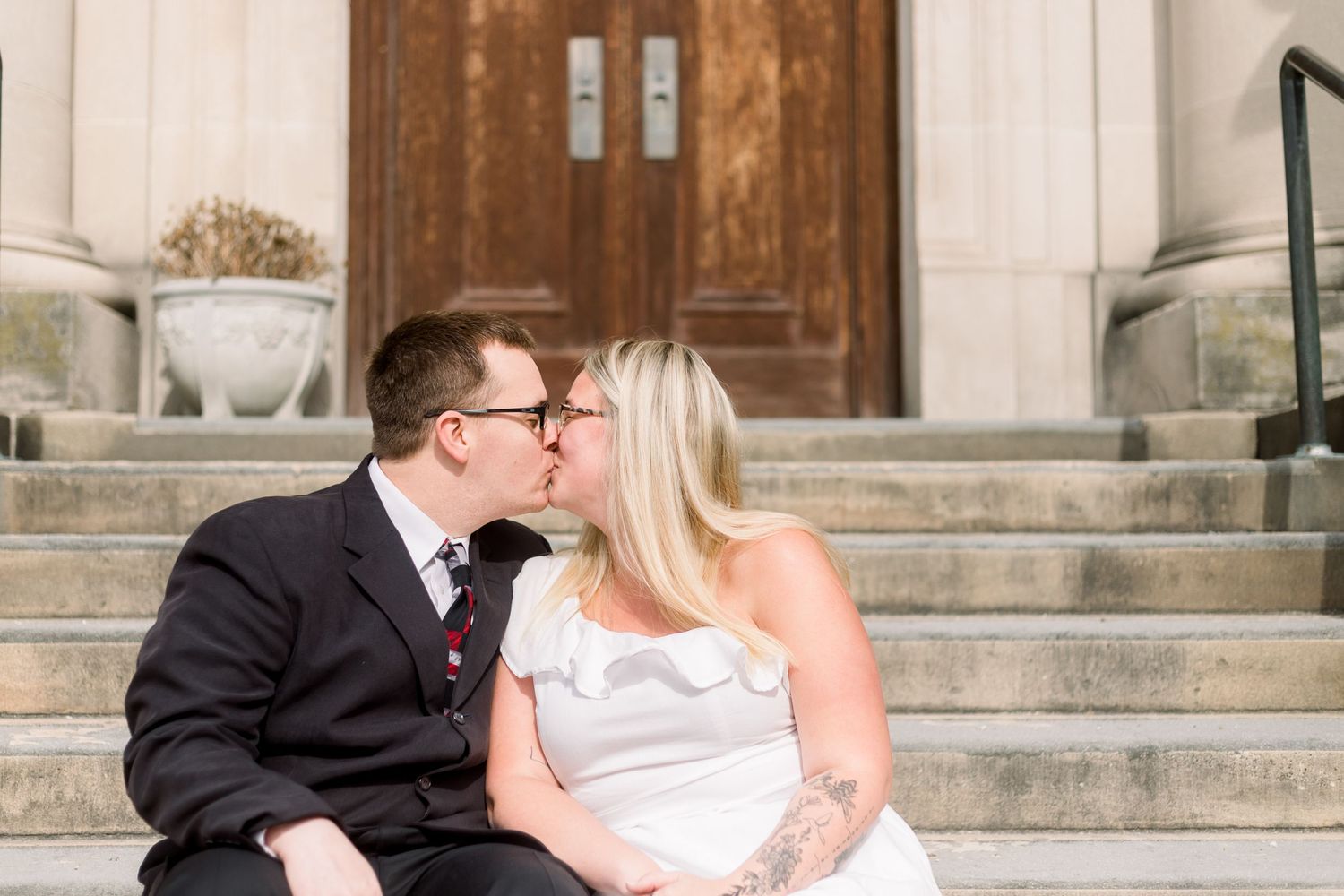 A couple shares an intimate moment while sitting on stone steps in front of a wooden door.