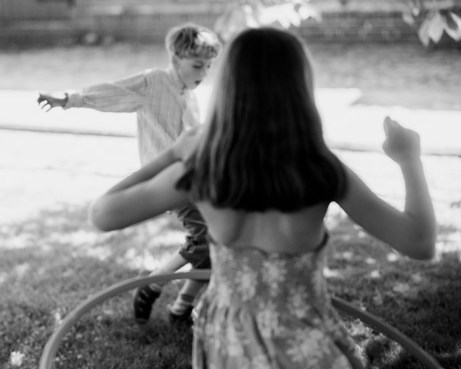 Black and white image of two children playing and spinning outdoors in summer.