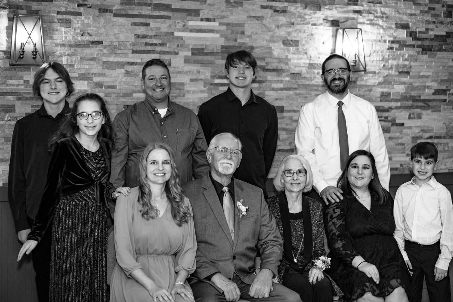 Multi-generational family portrait in formal attire against textured stone wall background.