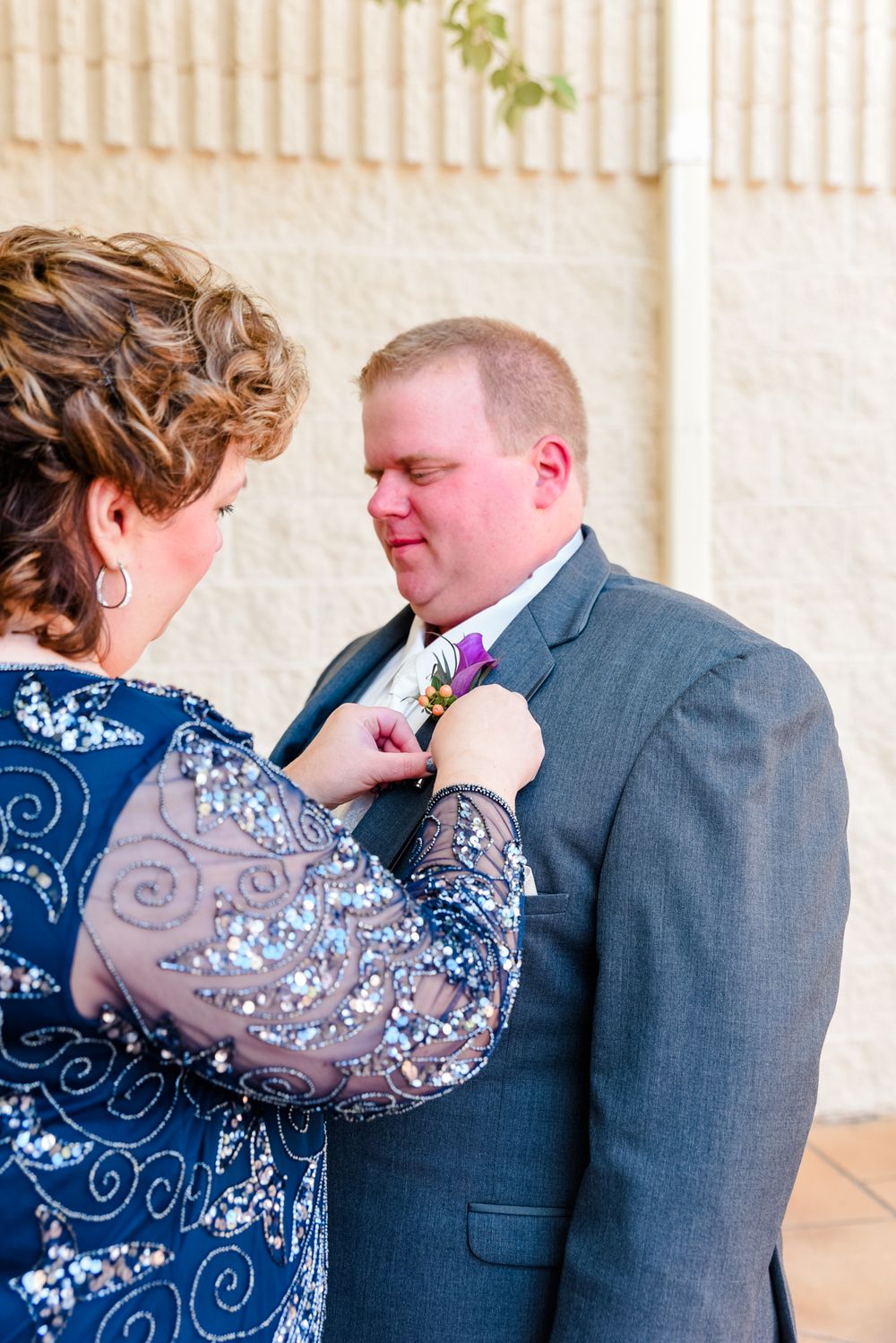Someone adjusting a boutonniere on a gray suit jacket during formal occasion.