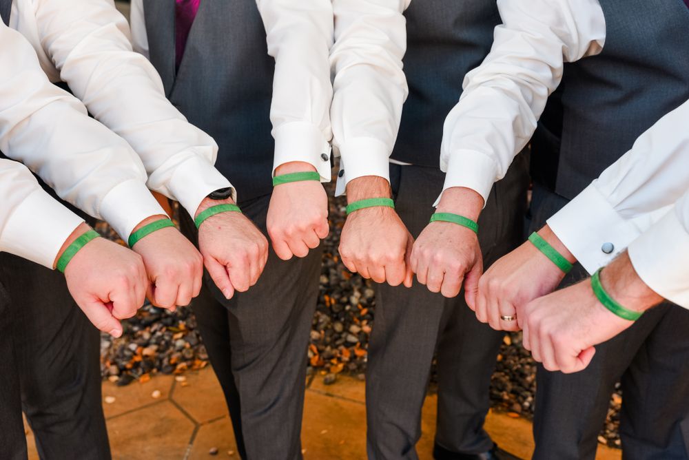Groomsmen showing off matching green and white wristbands at a wedding celebration.