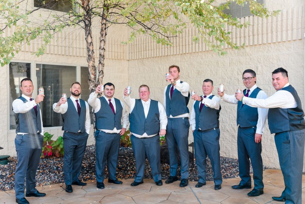 Wedding party in matching vests and ties posing together against a building exterior.