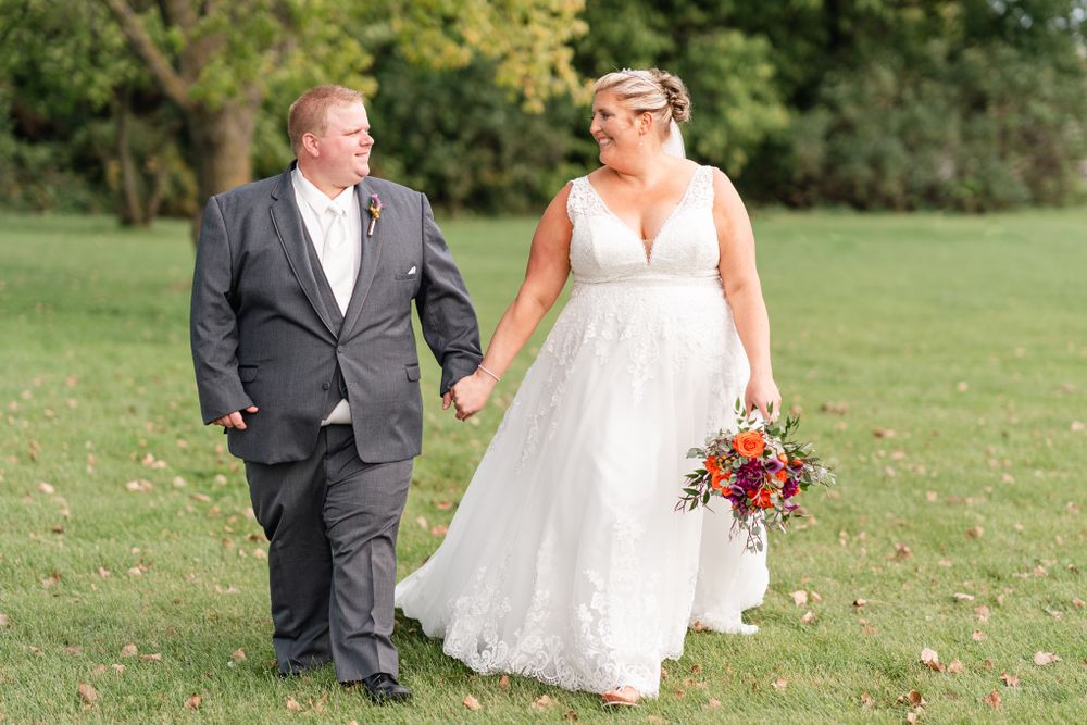 Romantic wedding couple strolling through green parkland with autumn foliage.