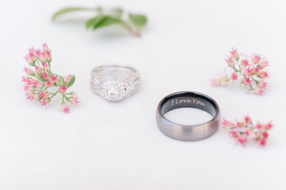 Wedding rings arranged with delicate pink flowers on white background.