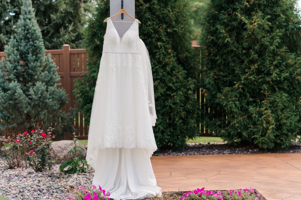 Elegant white wedding dress hanging outdoors against garden backdrop.