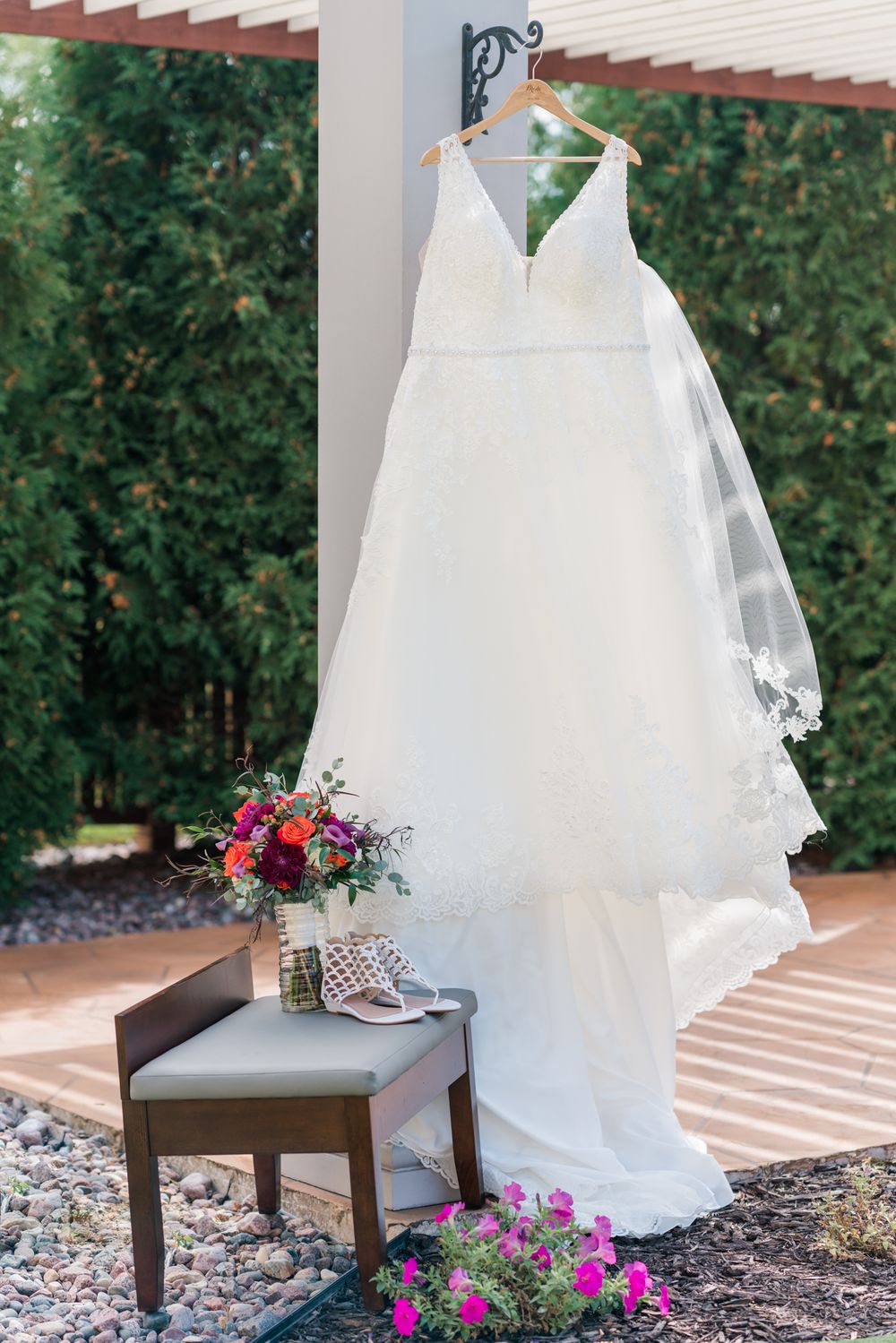 White wedding gown displayed with veil and floral bouquet on rustic bench.