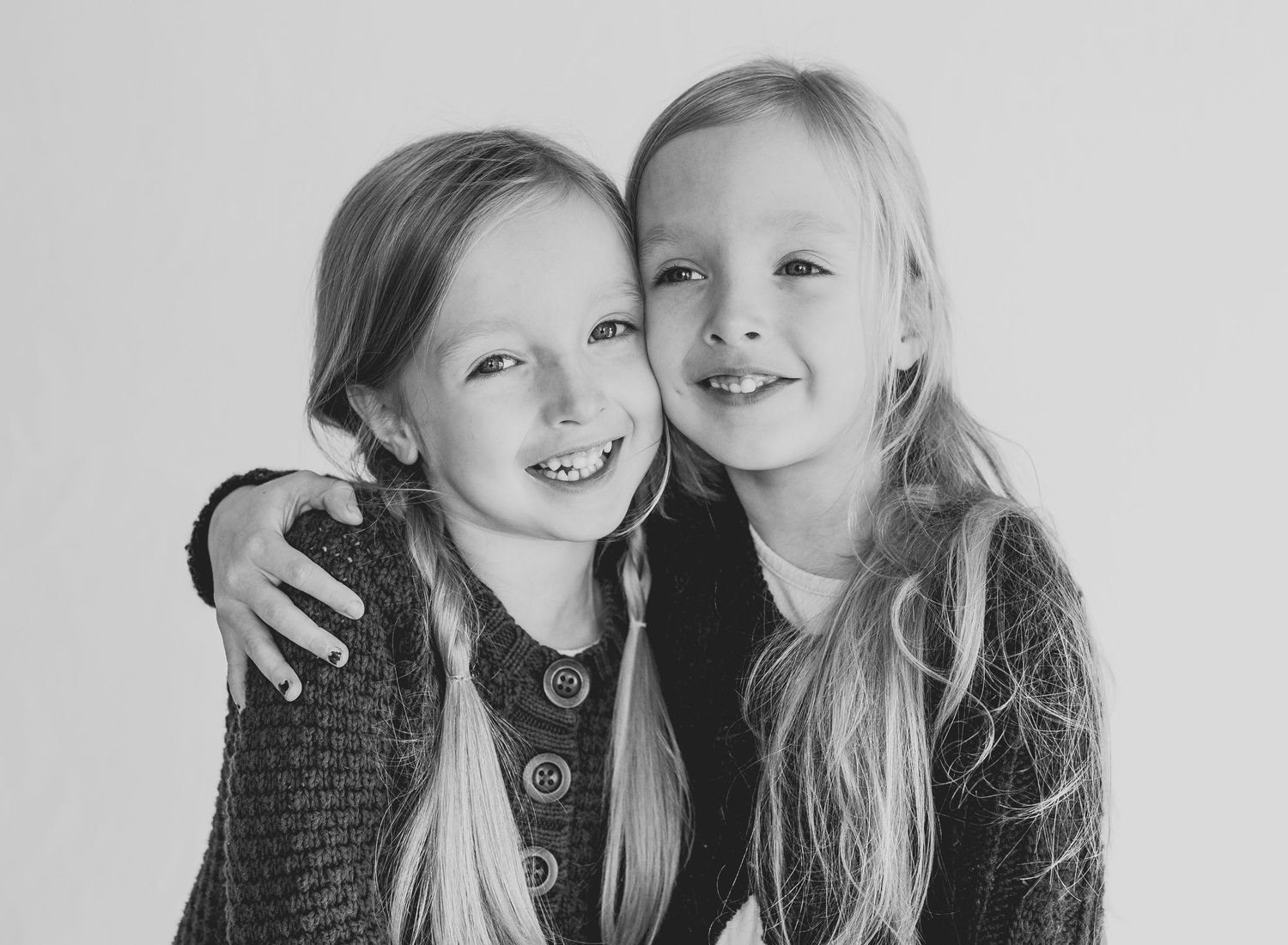 Two girls with long hair embracing and smiling in black and white portrait.