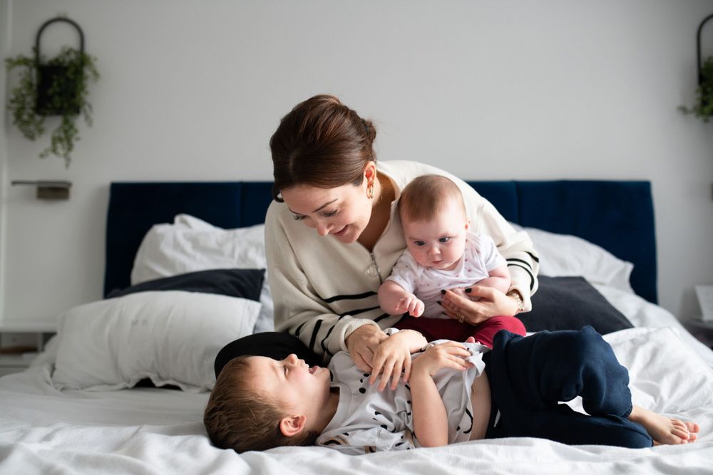 Mum and her two little ones having some cuddles and fun on the bed, during an at home newborn photoshoot, Ashtead Surrey