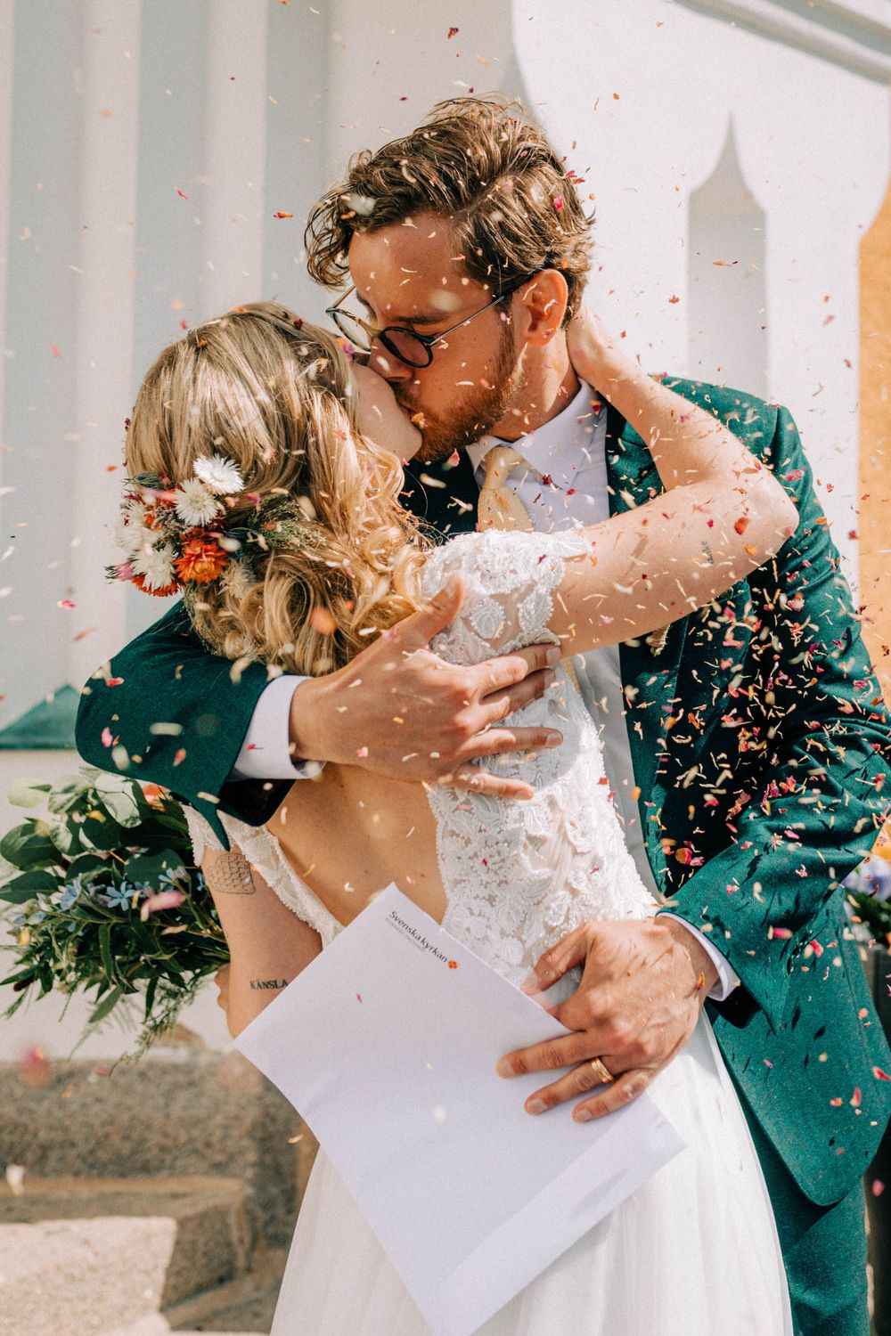A romantic wedding kiss moment with confetti falling around the couple in beautiful sunlight.