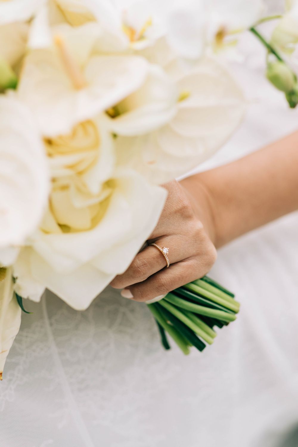 Close-up of a bride's hand holding an elegant white calla lily bouquet with wedding ring visible.
