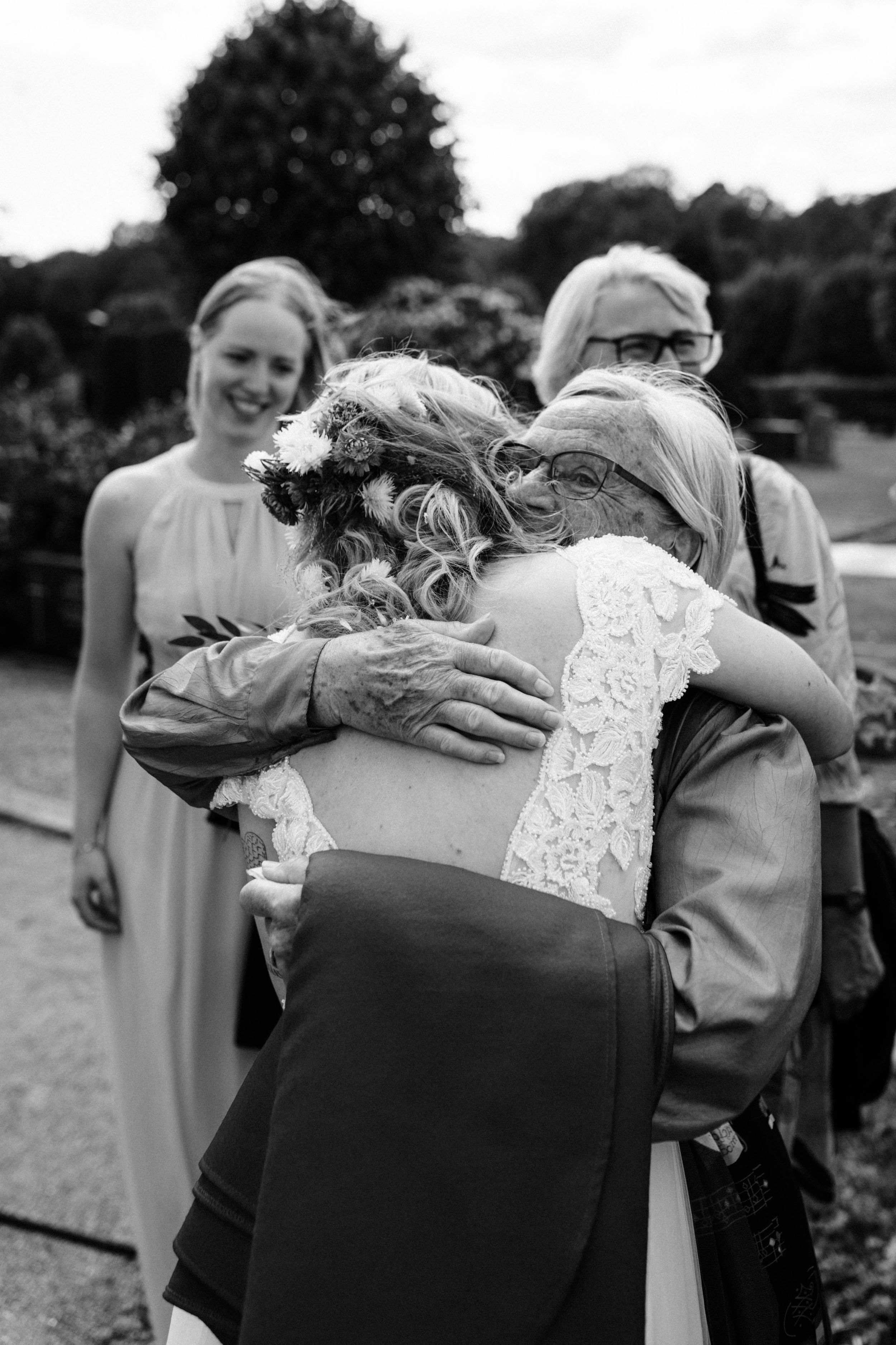 An emotional black and white photograph capturing warm embraces at a wedding celebration.