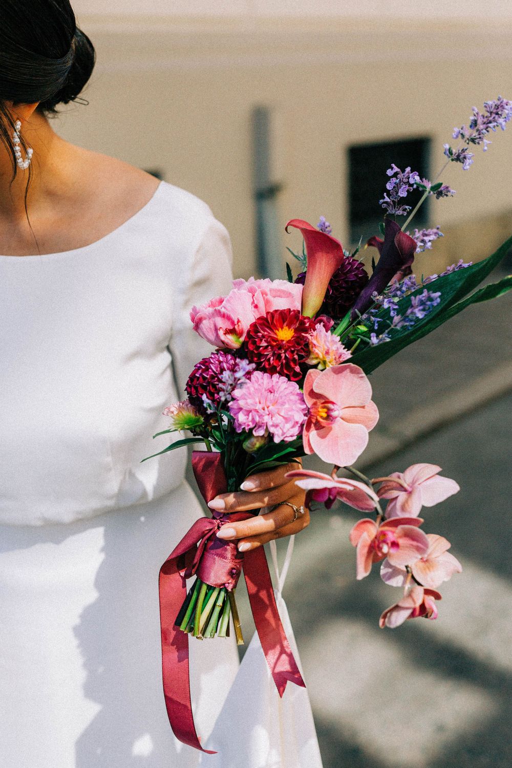 Close-up of a colorful bridal bouquet with pink flowers and purple accents tied with a ribbon.
