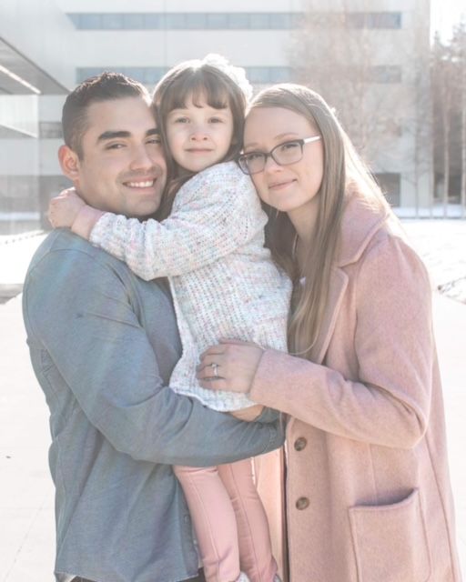 Family of three posing together outdoors in winter wearing coordinated casual attire.