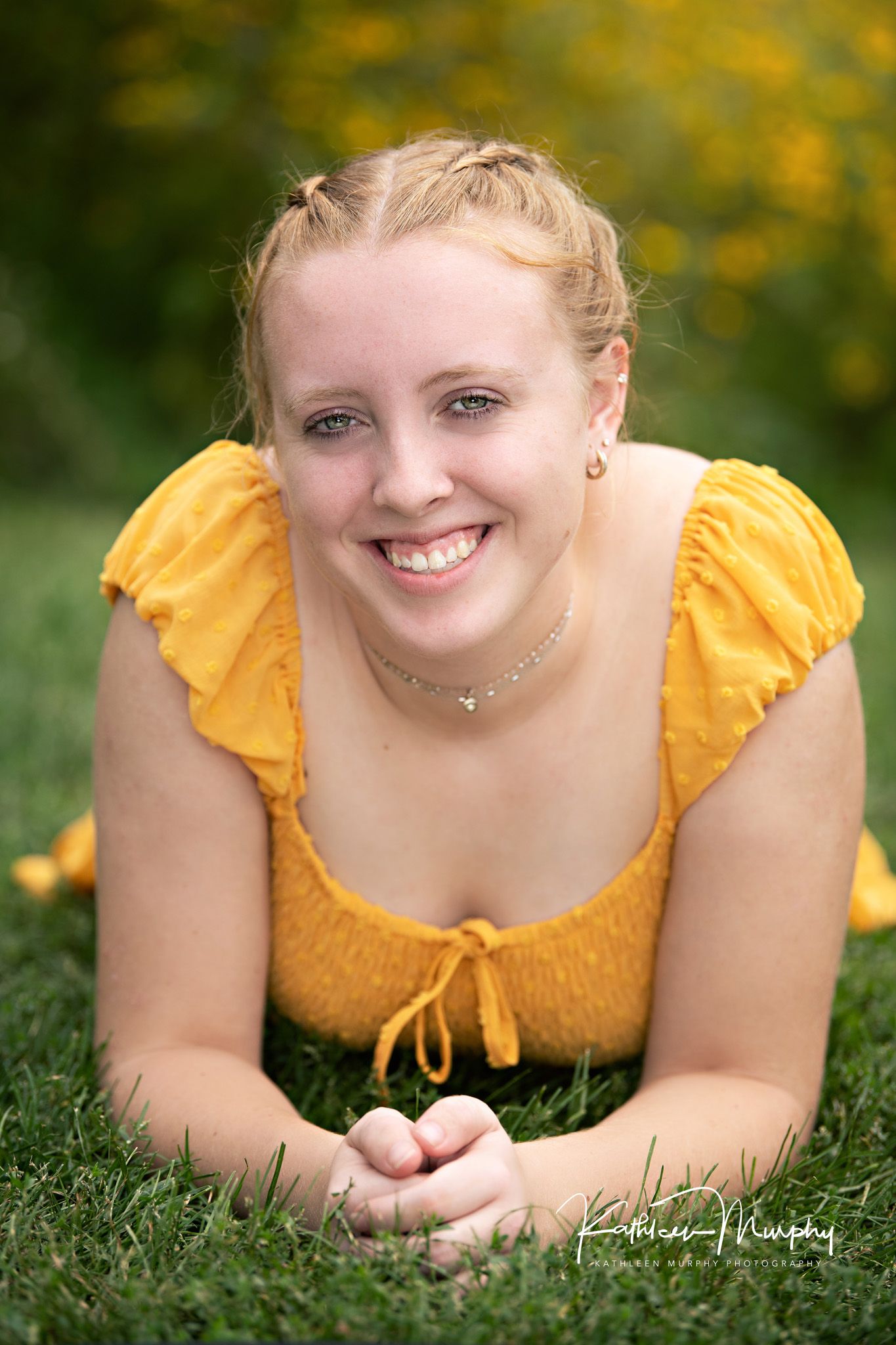 Portrait of someone in a bright yellow top lying on grass with yellow flowers in the soft-focus background.
