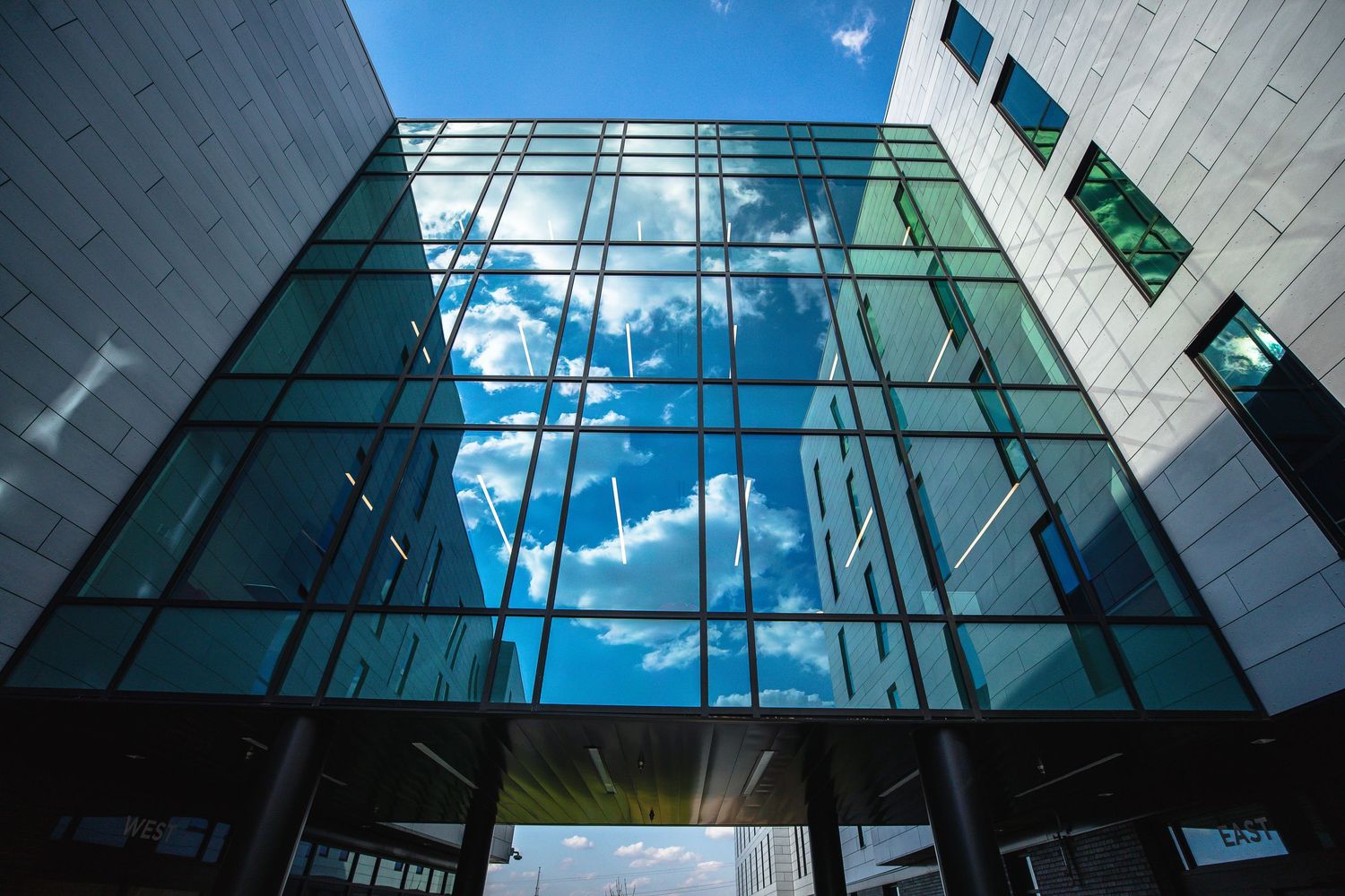 Modern glass building facade reflecting blue sky and clouds.