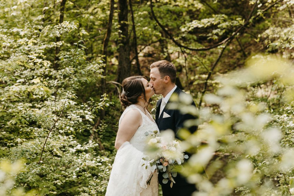 Bride and groom share an intimate moment framed by lush green foliage in a forest setting.