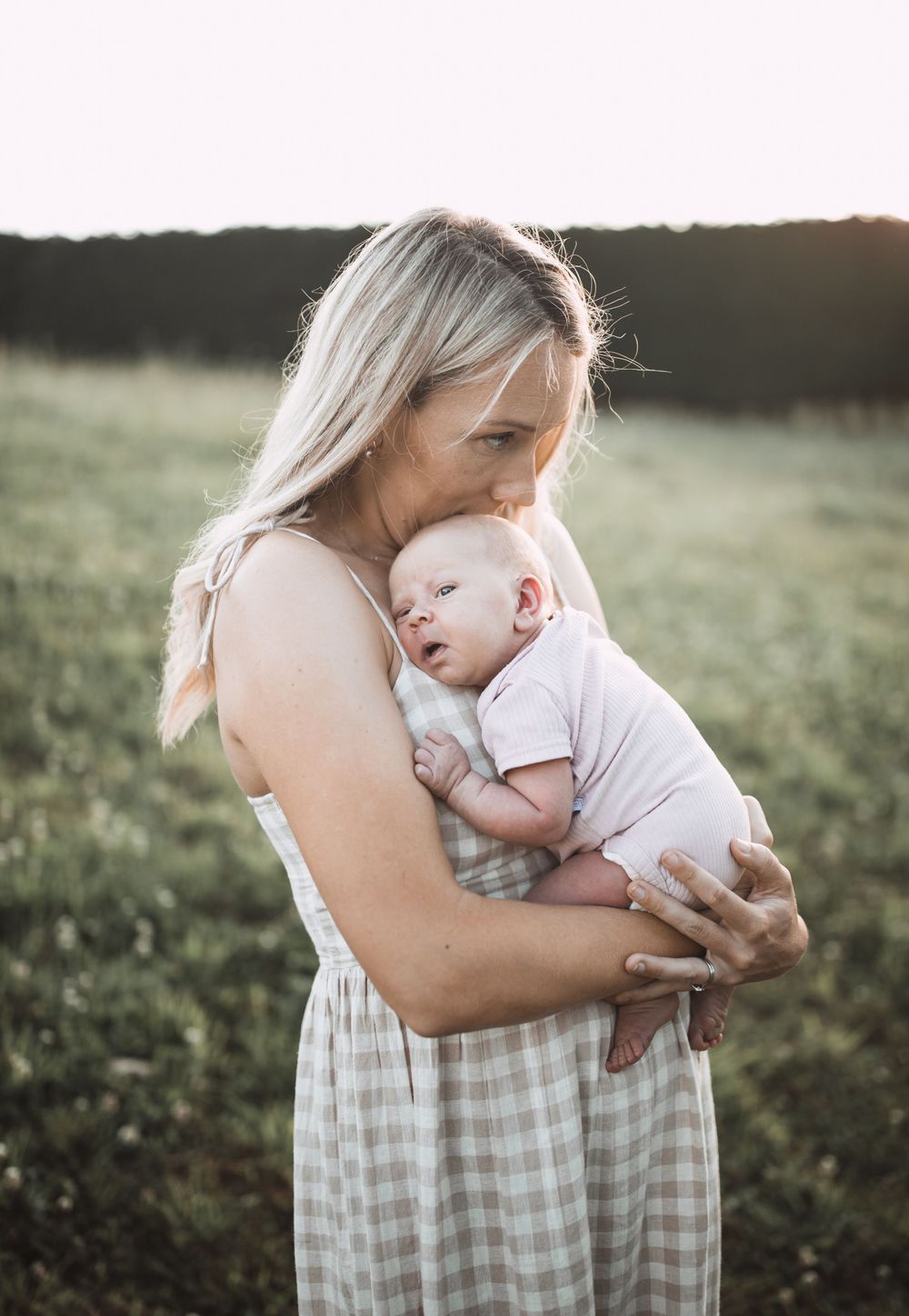 A tender moment between parent and baby outdoors in a grassy field at sunset.