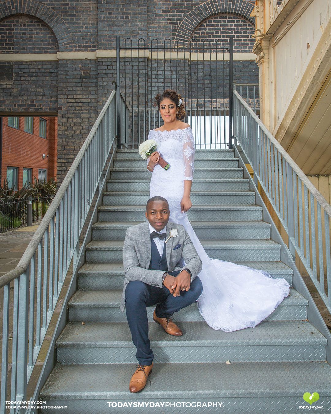 Elegant wedding portrait on industrial metal staircase with brick wall backdrop.