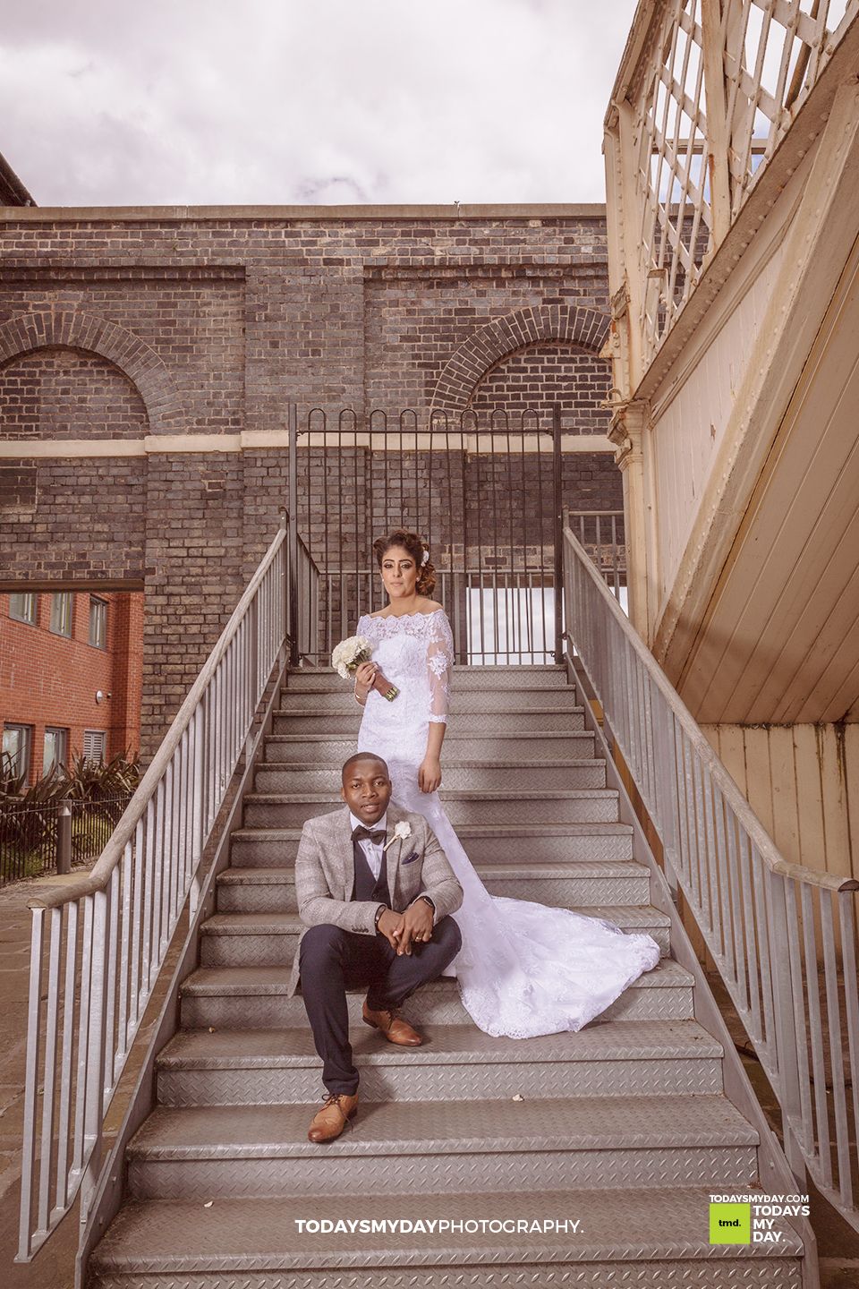 Wedding couple posing dramatically on industrial brick and metal staircase.