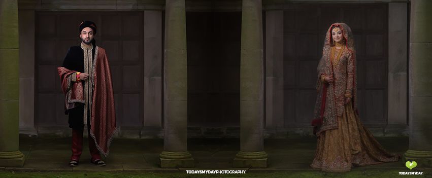 Two people in medieval style costumes standing in dramatic lighting against stone columns.